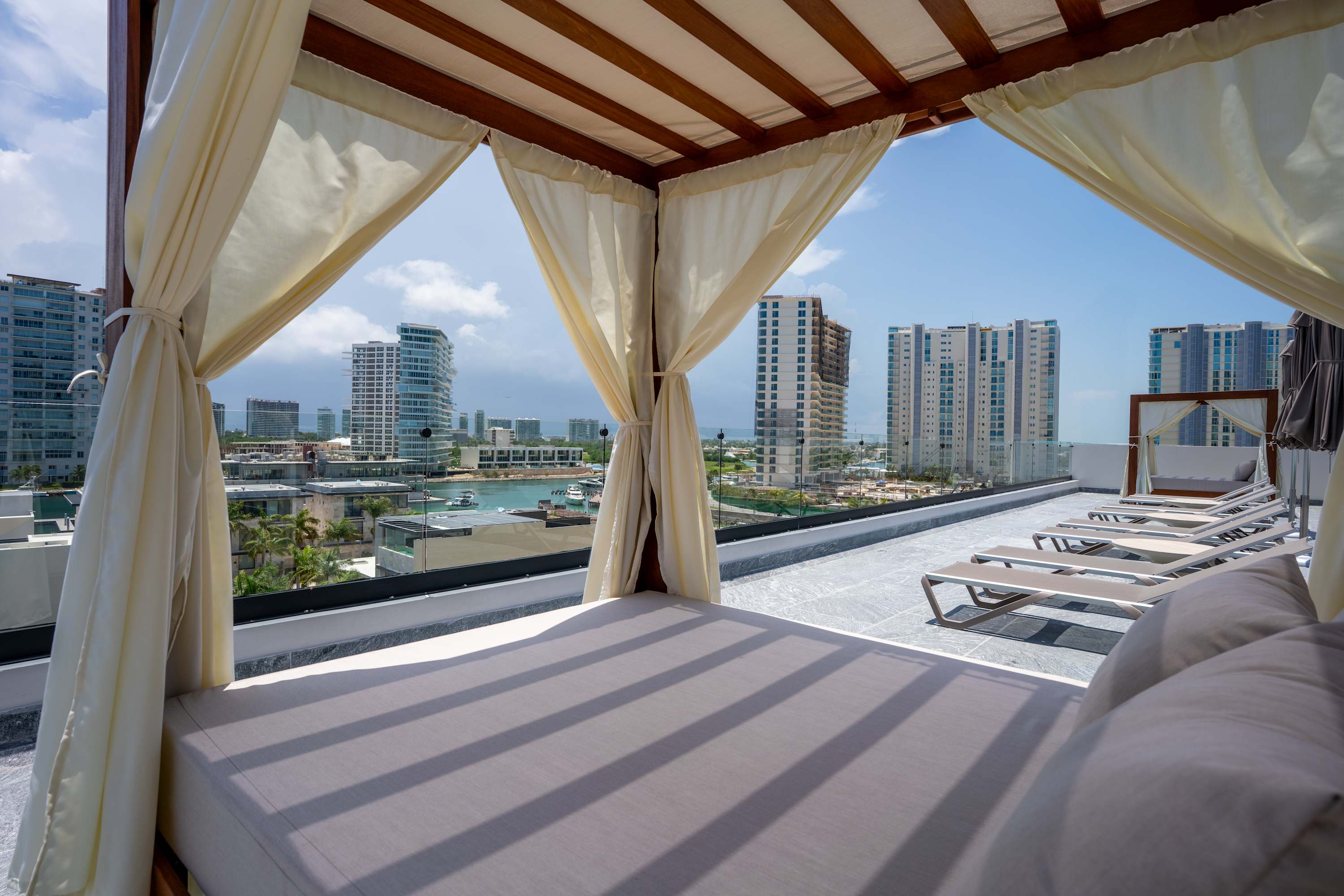 Covered daybed on rooftop patio with lounge chairs and city views.
