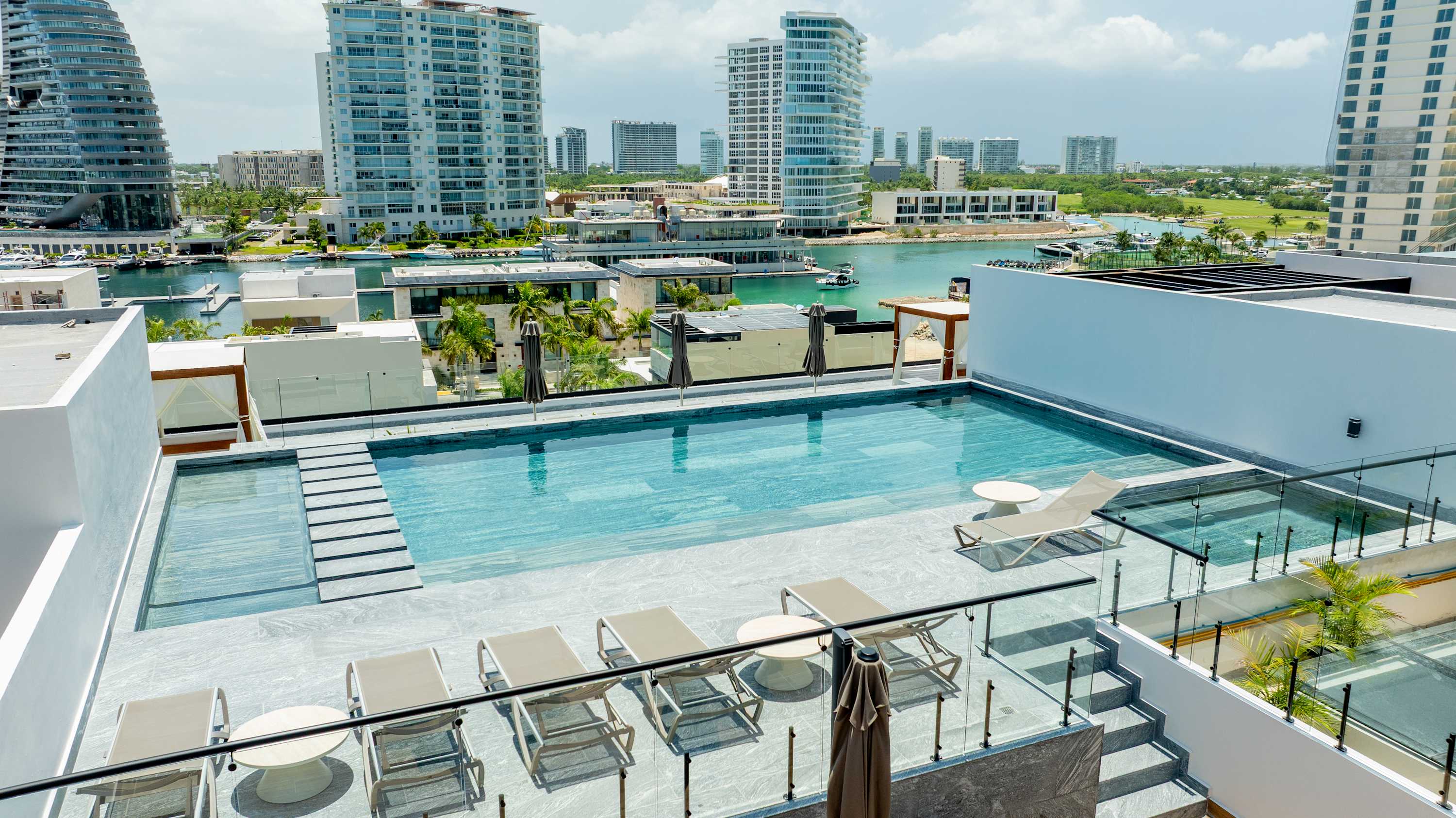 Rooftop pool with loungers overlooking a waterfront city skyline and yachts.