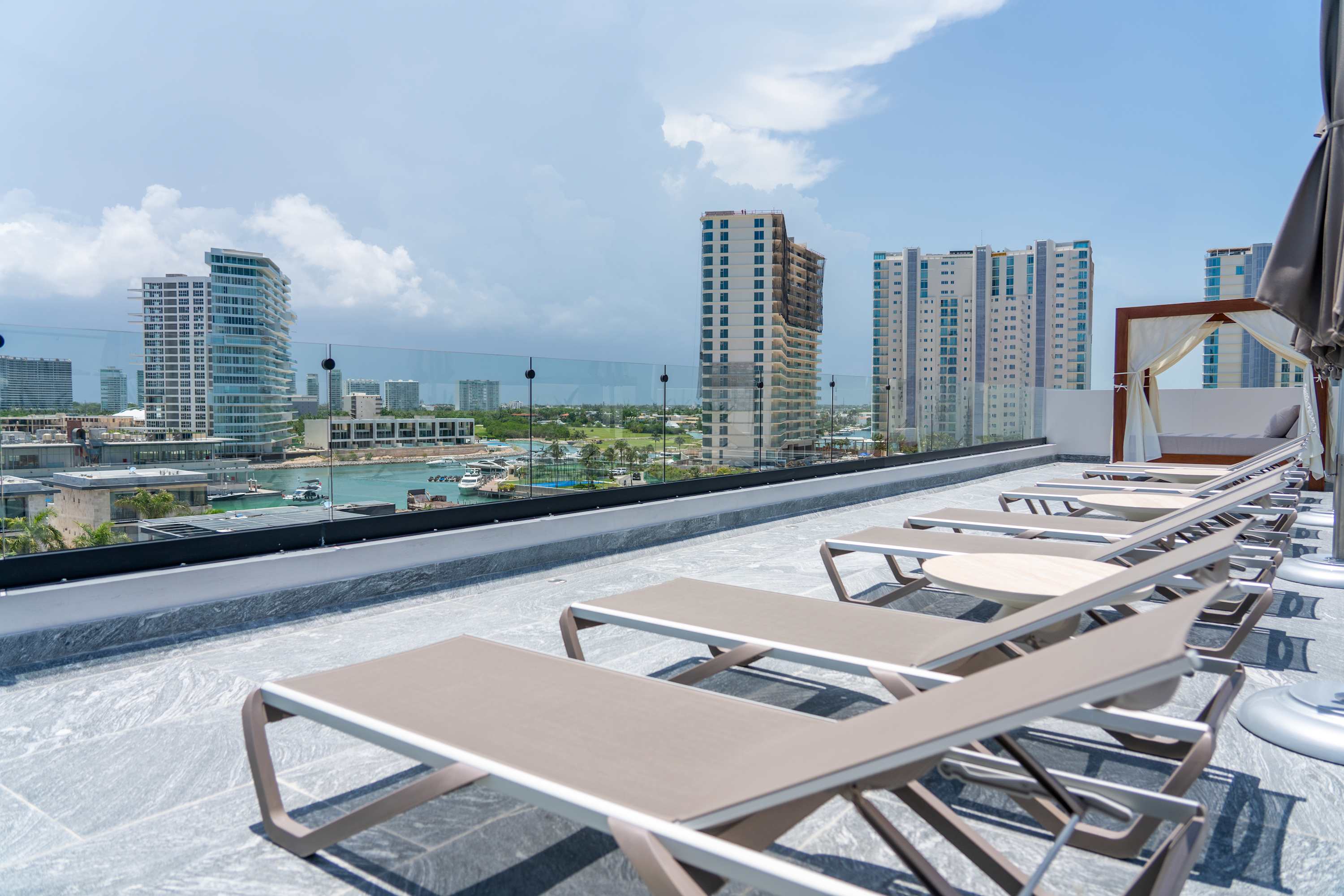 Rooftop lounge chairs with a view of modern buildings and a harbor.