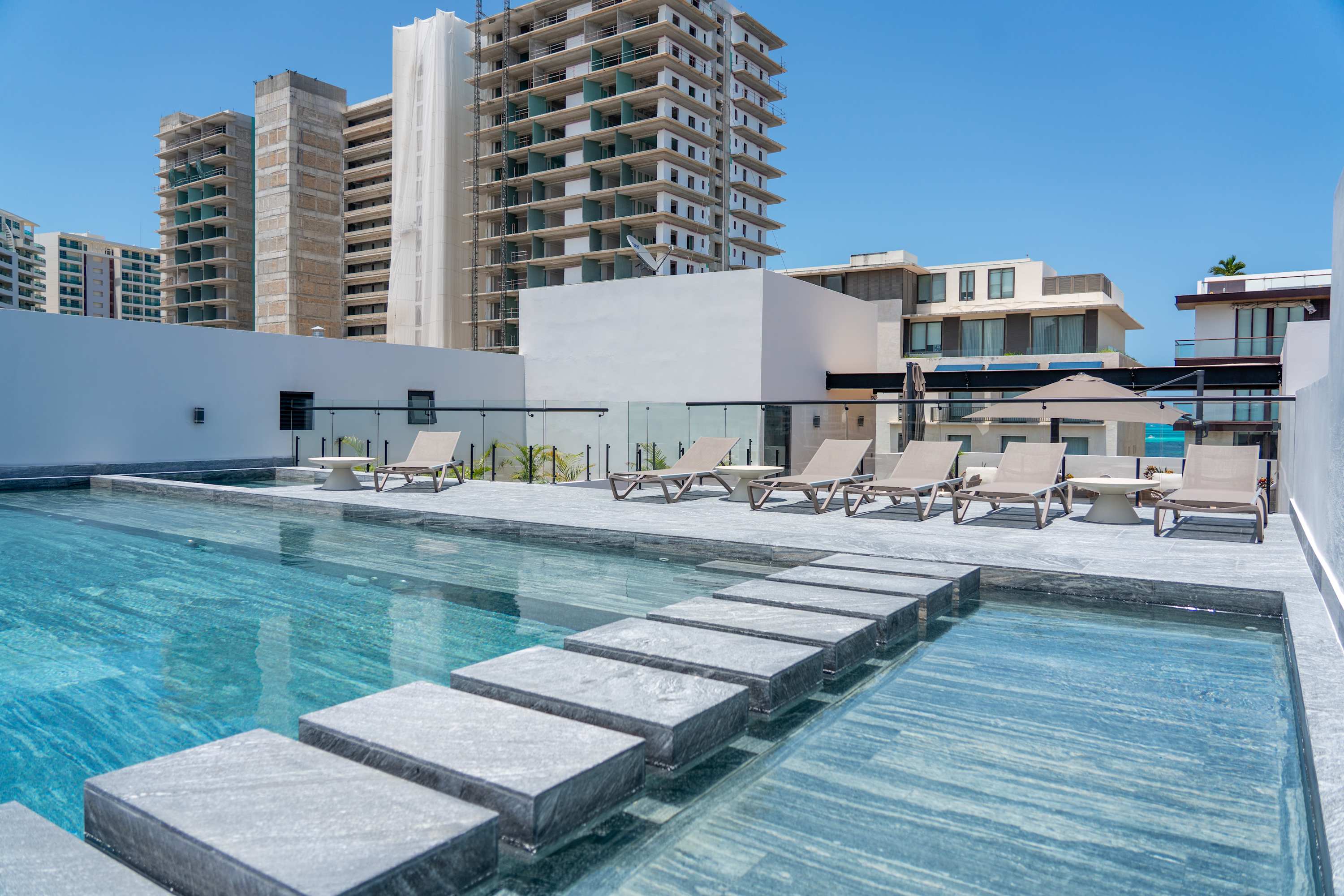 A rooftop pool with lounge chairs and buildings under construction in the background.
