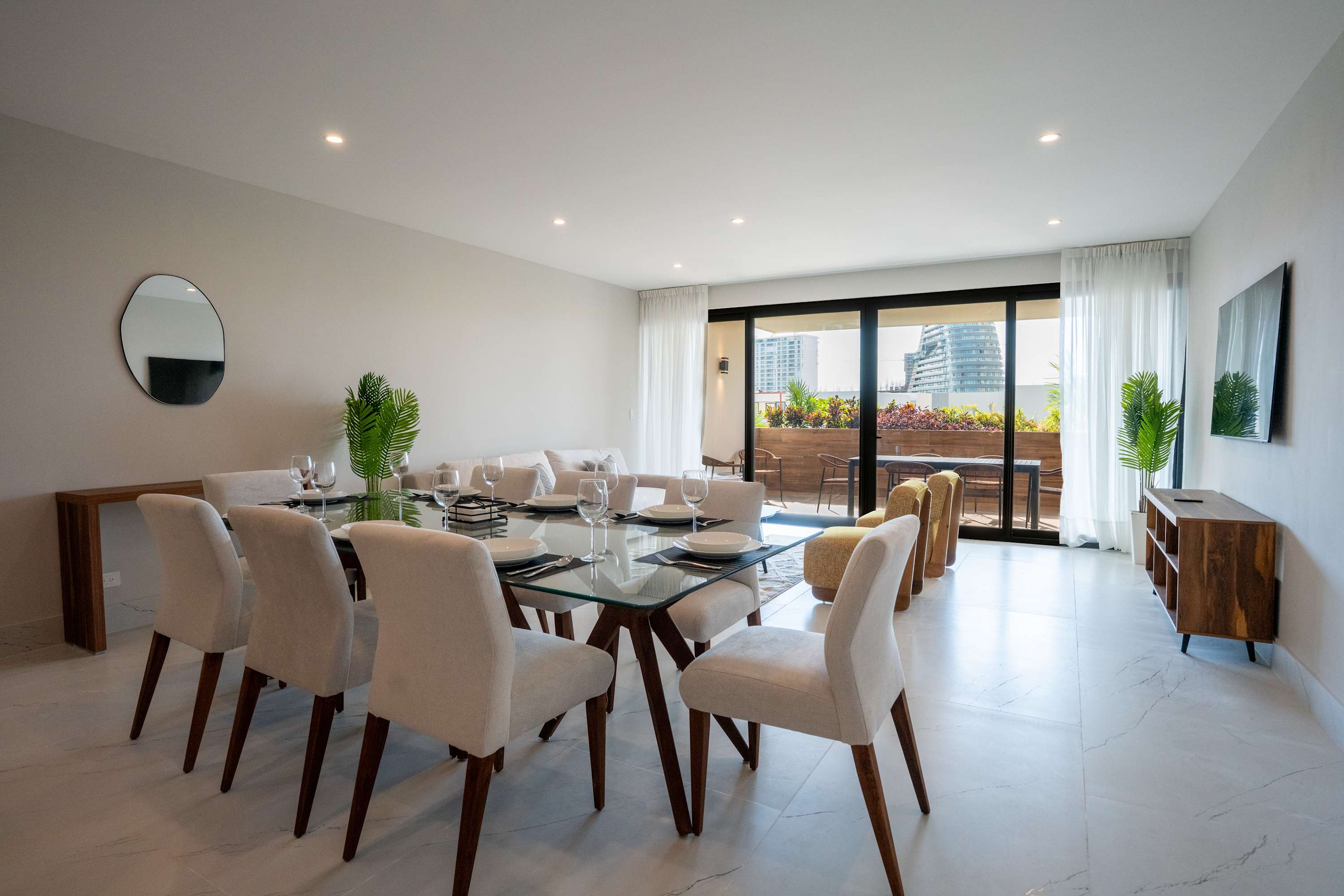 A modern dining room with a glass-top table, chairs, and balcony views.