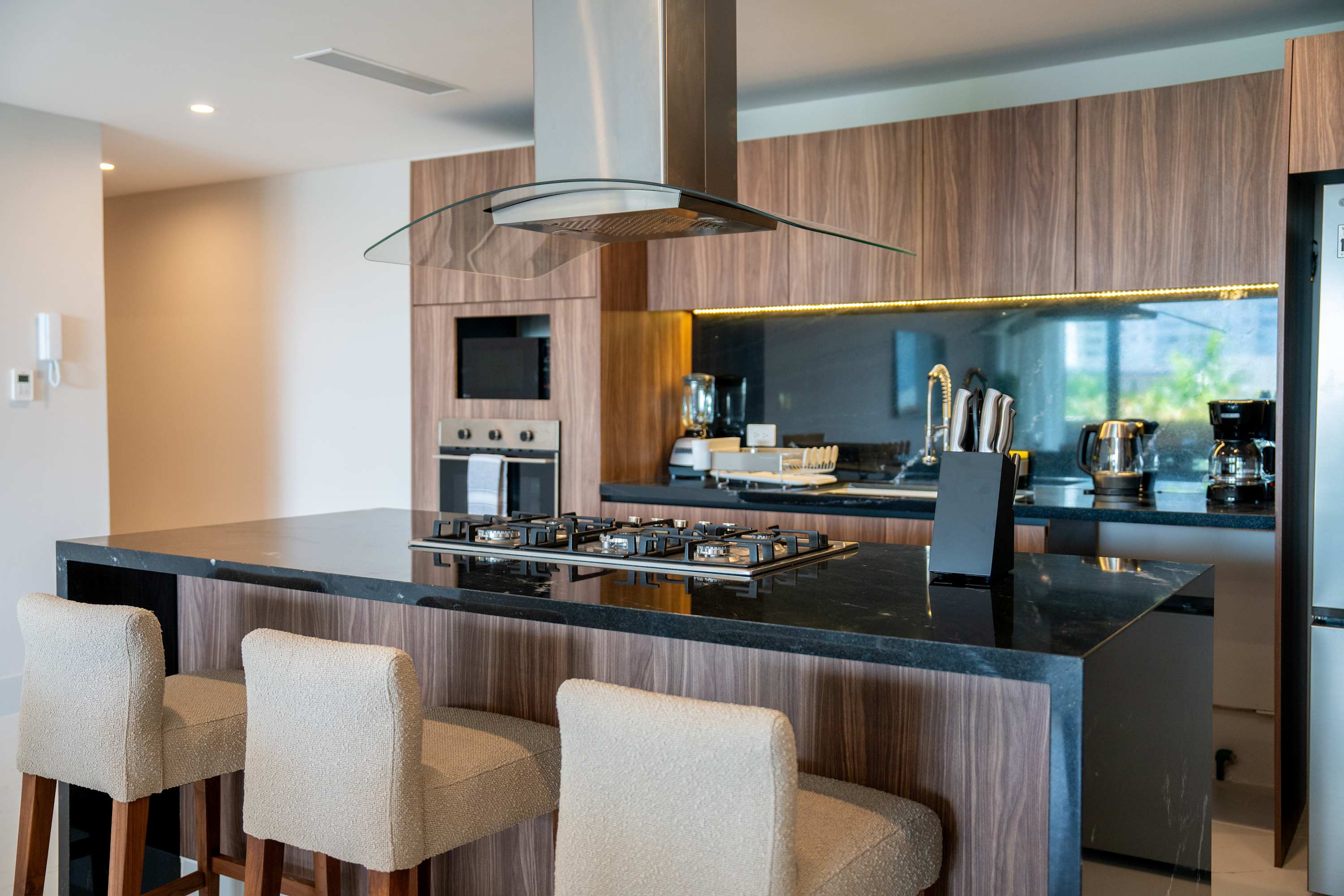 A modern kitchen with wood cabinets, granite countertops, and a breakfast bar with three stools.