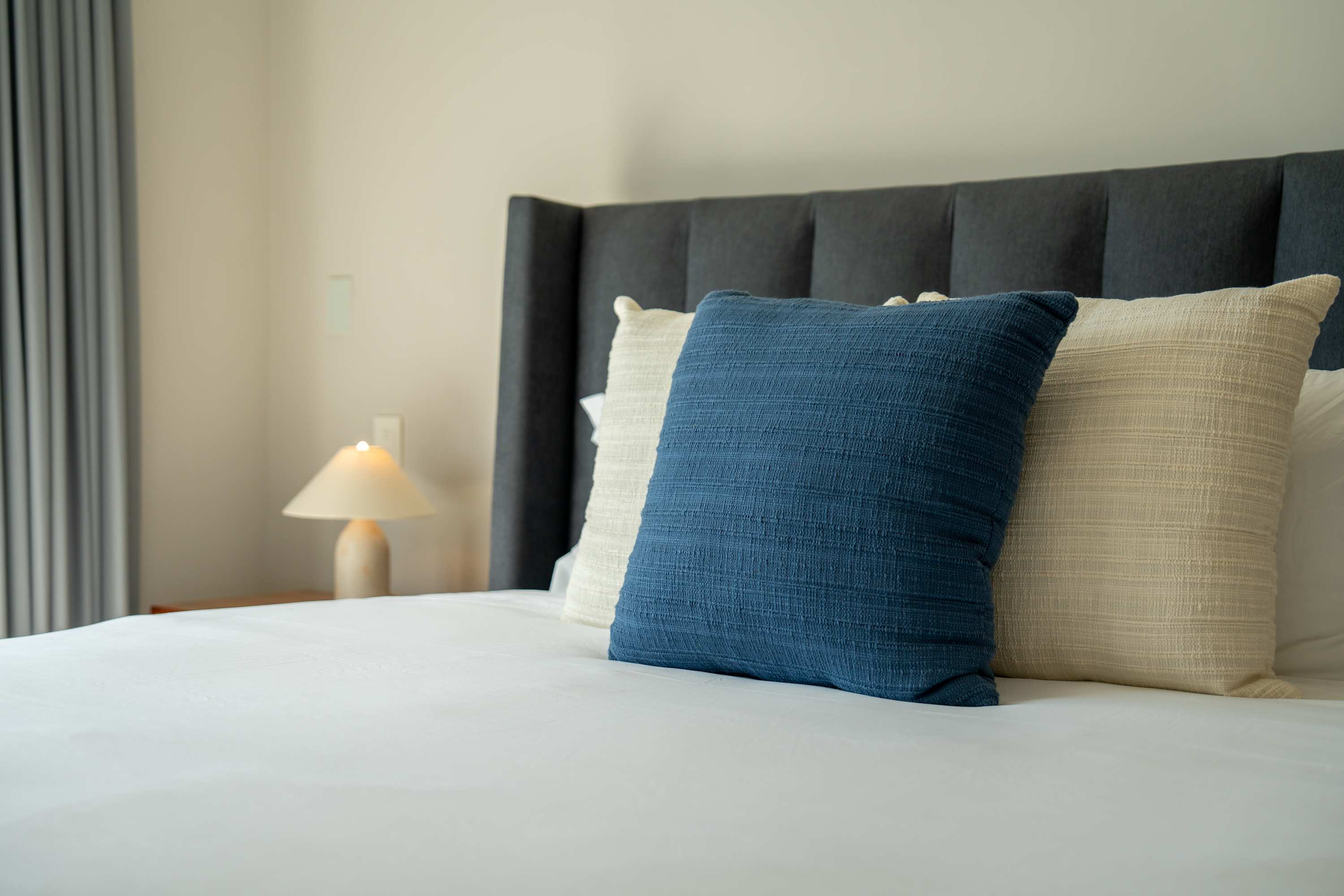 A close-up of a bed with a dark gray headboard and three pillows.