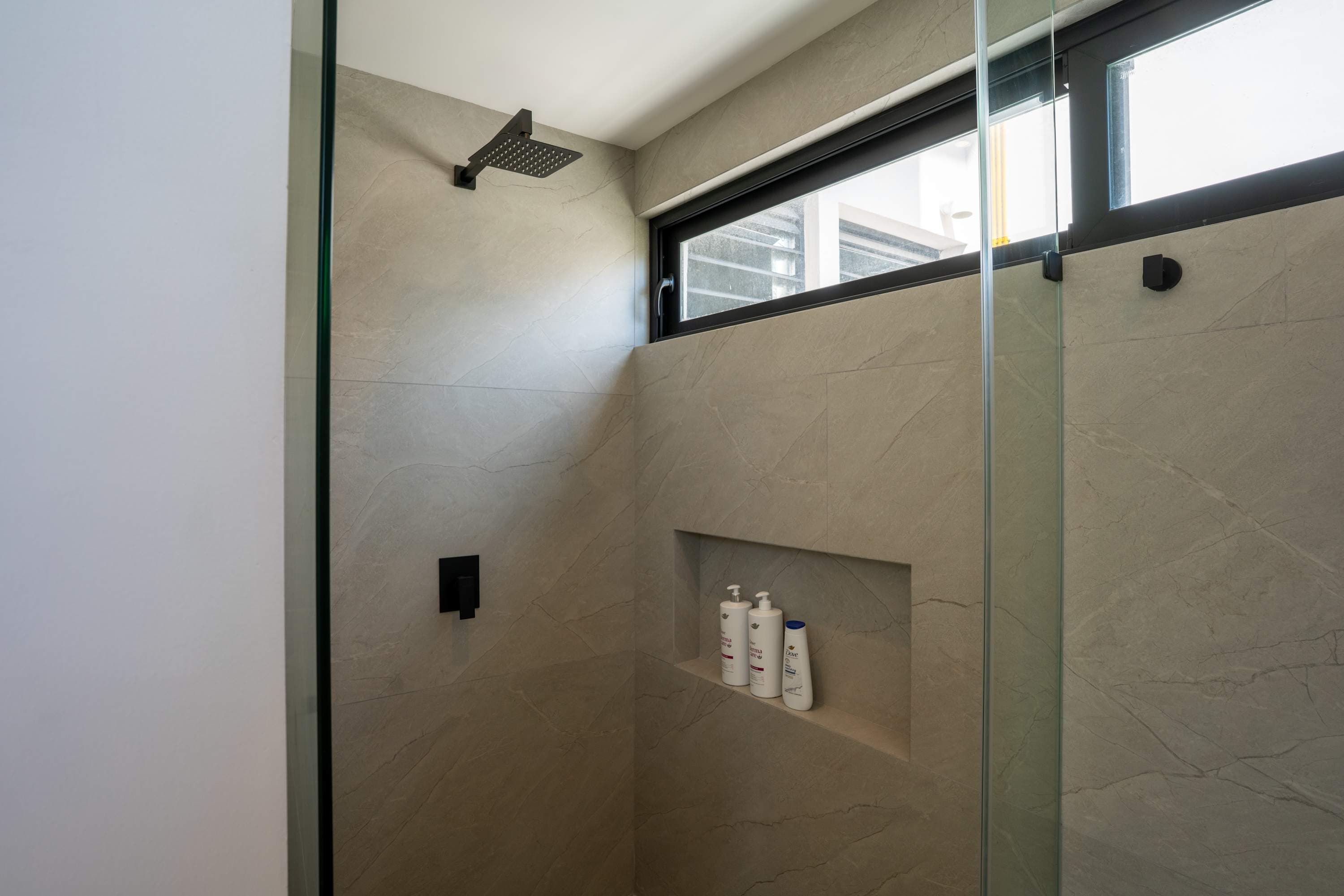 Modern shower with square shower head and embedded shelf with toiletries.