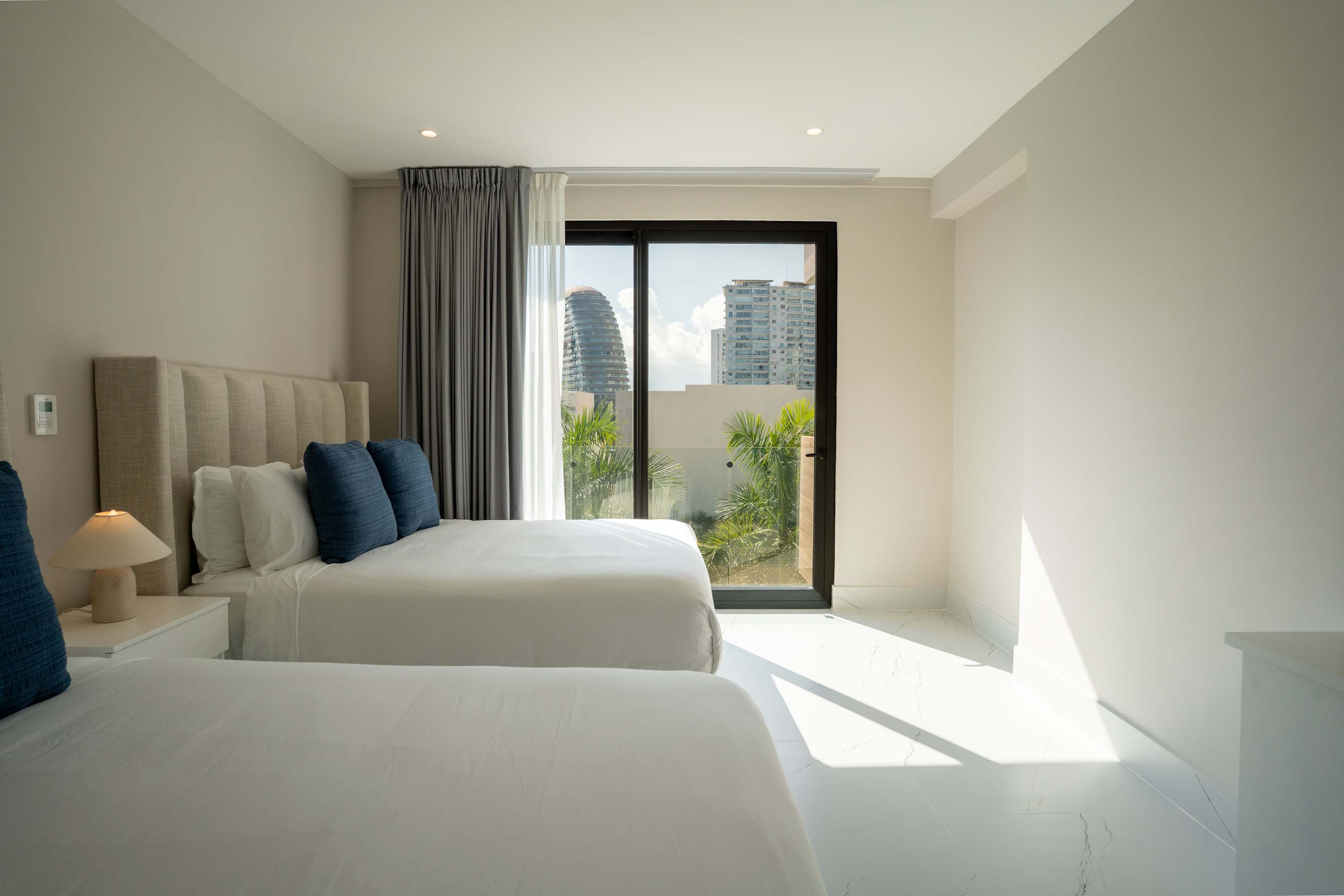 A modern bedroom with two beds and large windows offering a city view.