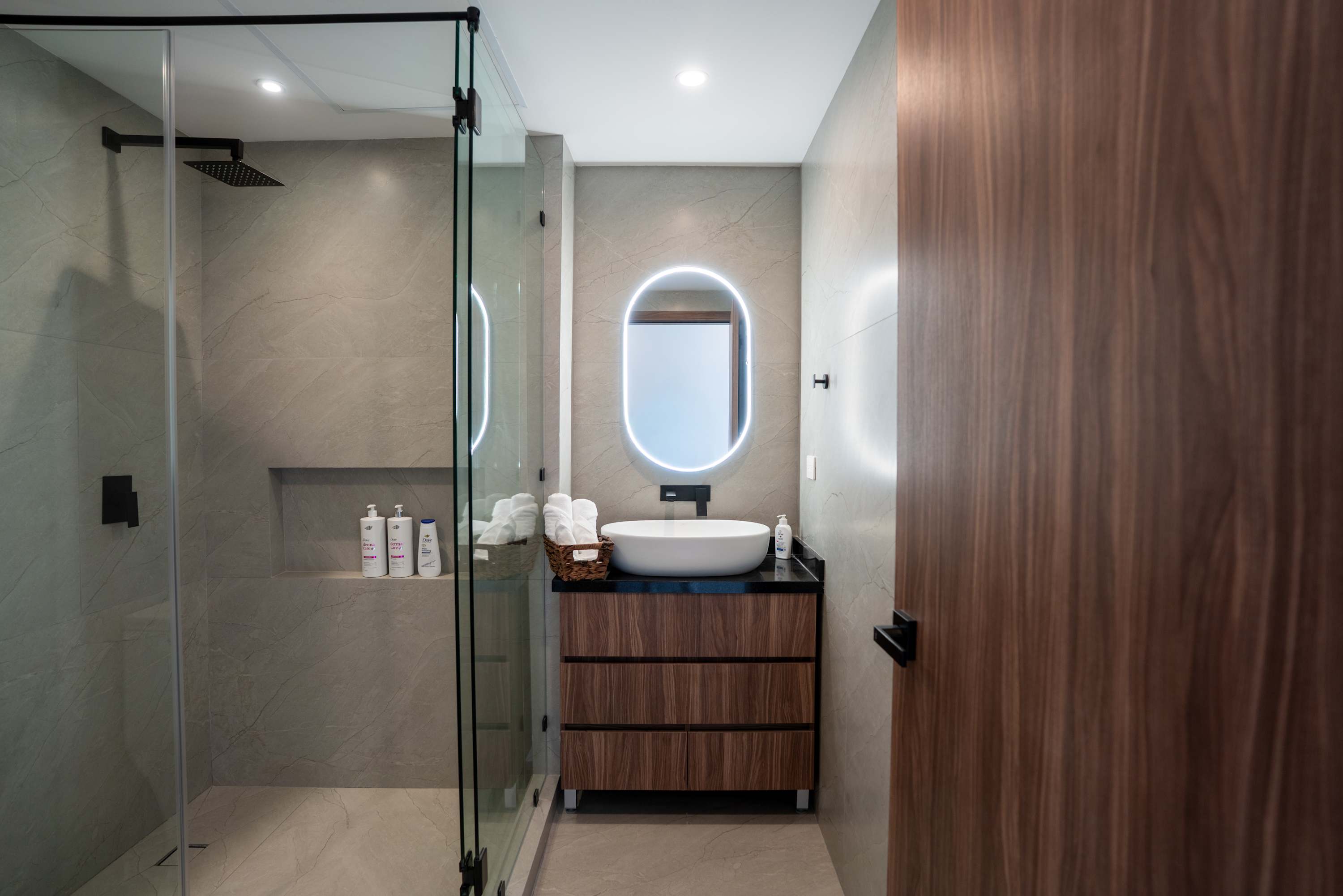 A modern bathroom with a glass-enclosed shower, a vanity with a sink and mirror, and a wooden door.