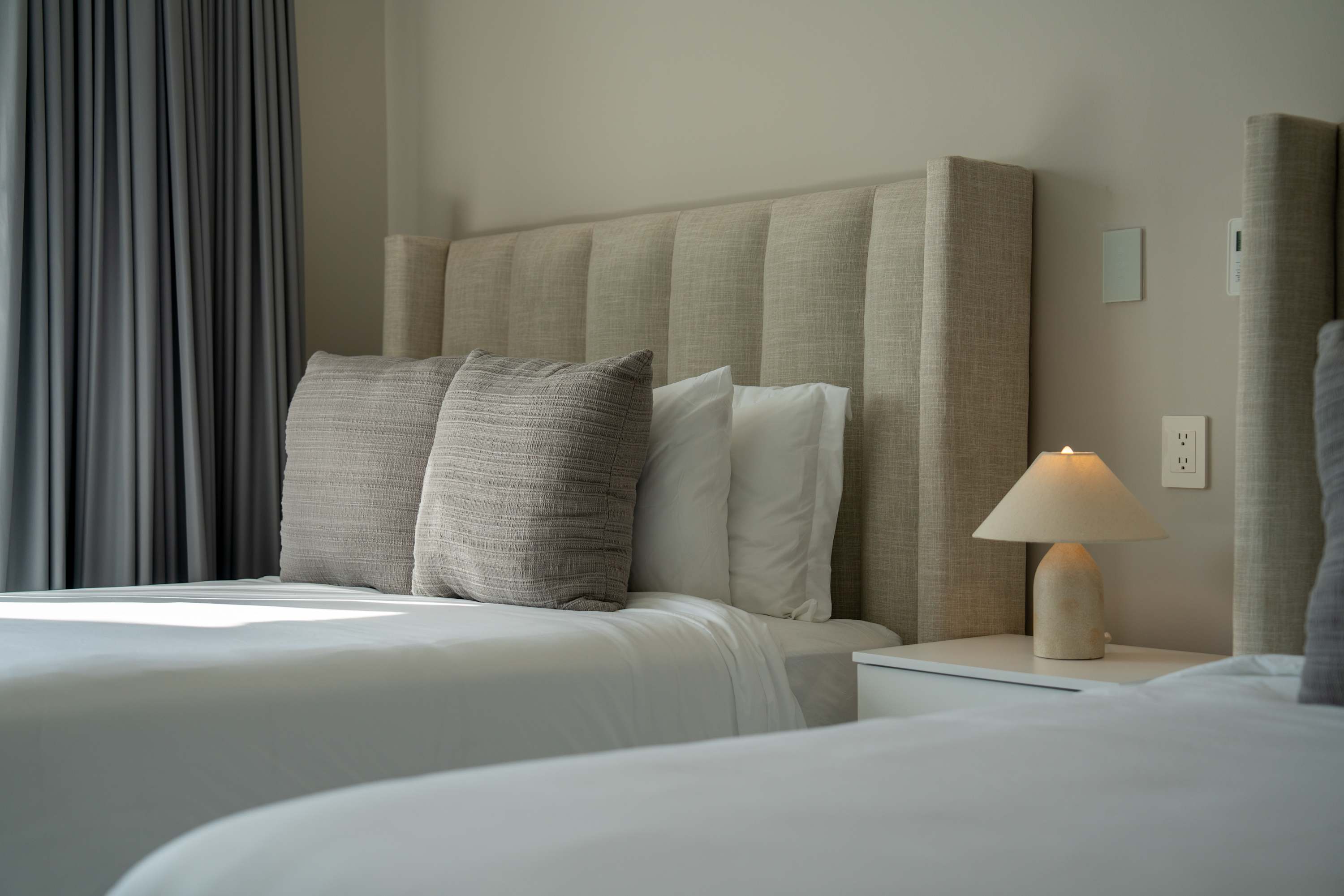A bedroom with two beds, a bedside lamp, and grey curtains.