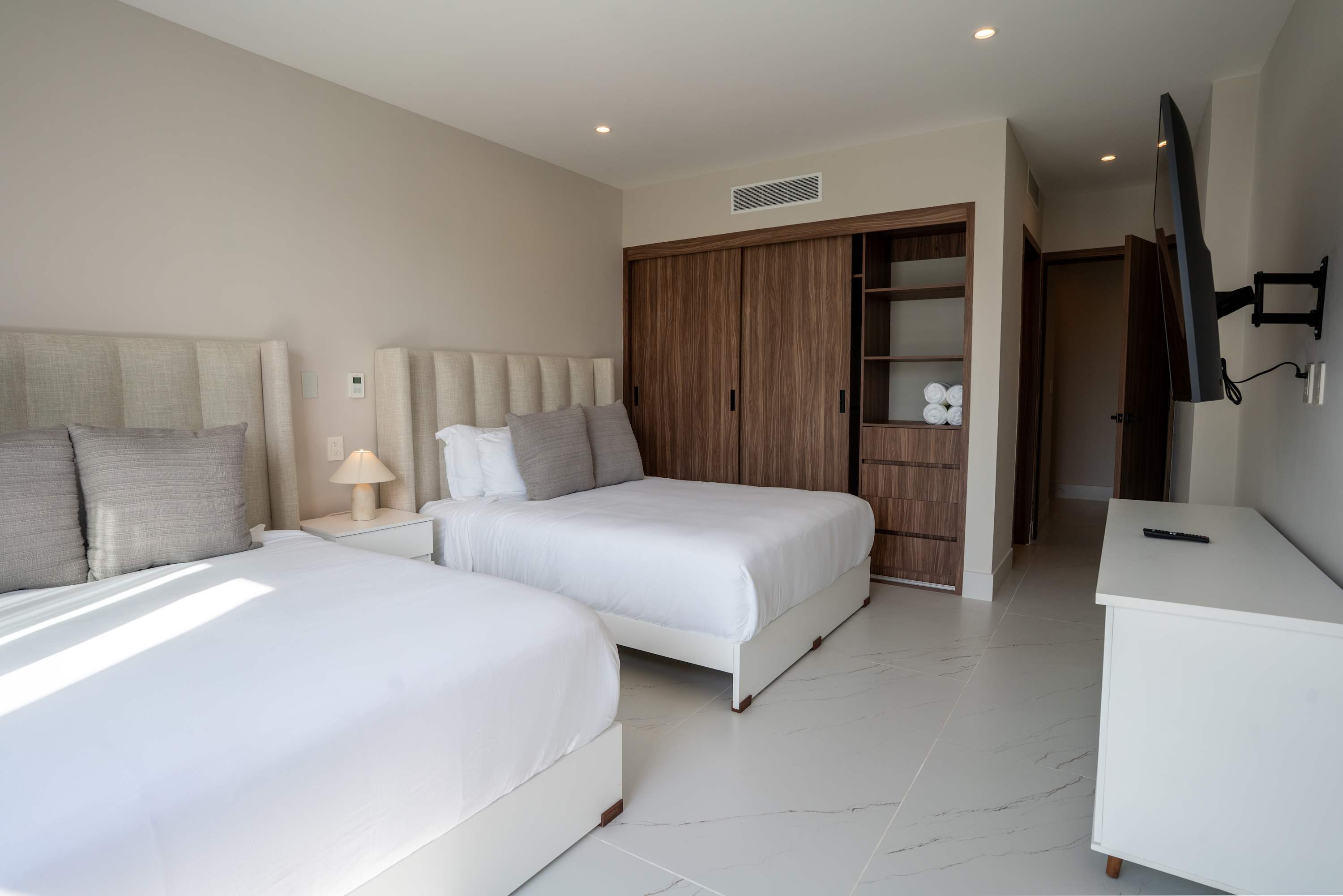 Two beds with white linens and gray pillows in a modern bedroom.