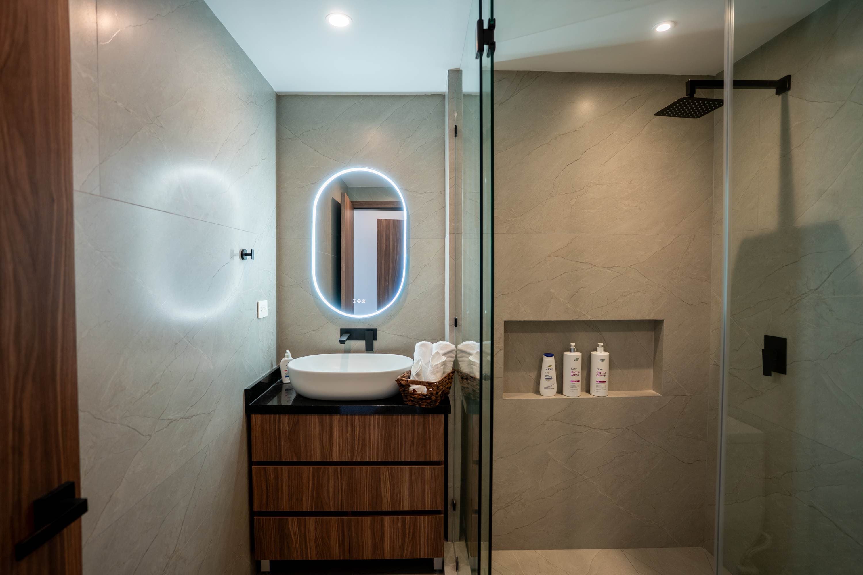 Modern bathroom with a lighted mirror, vessel sink, wood vanity, and glass-enclosed shower.