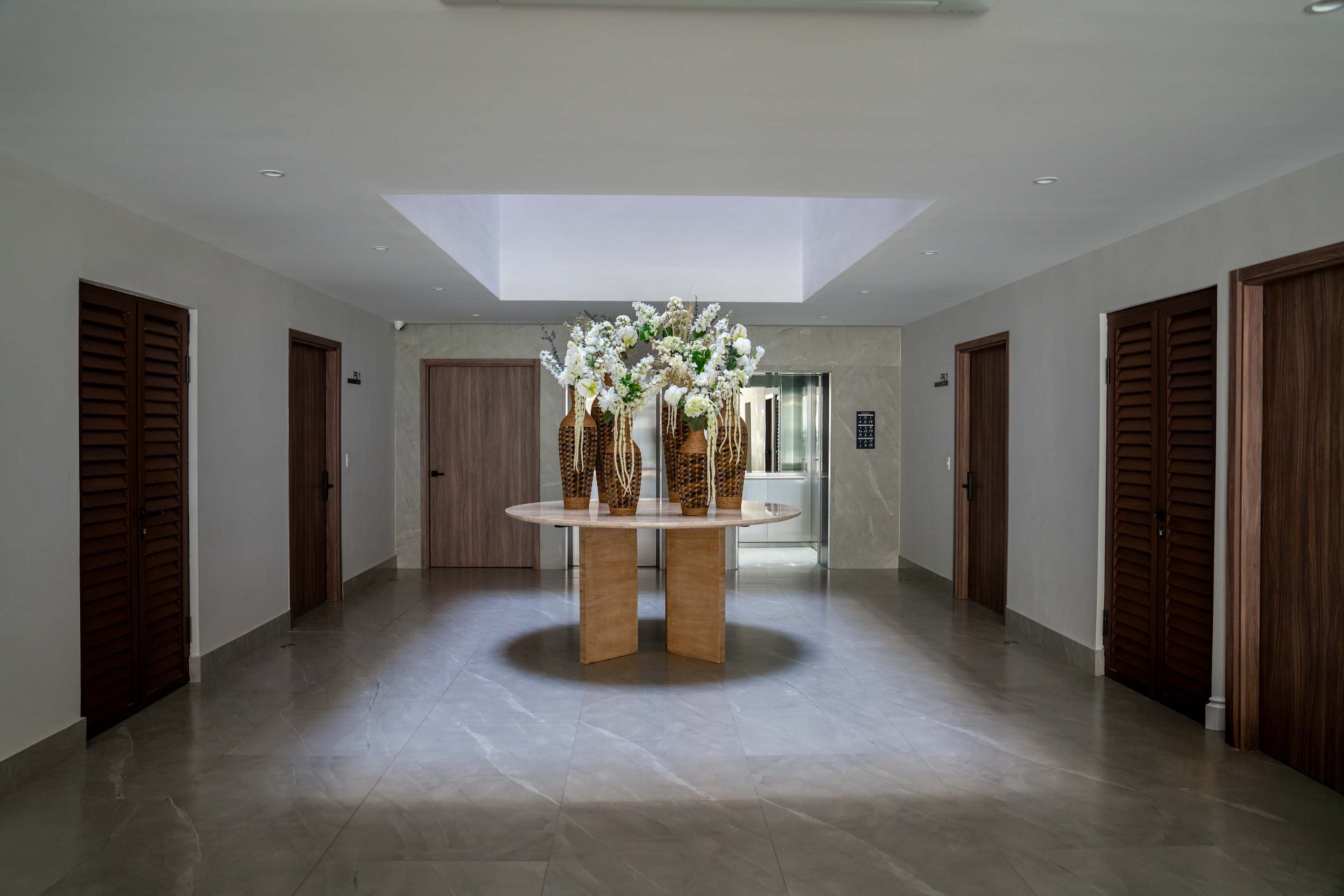 Foyer with a round table adorned with vases of flowers, a skylight, and doors.