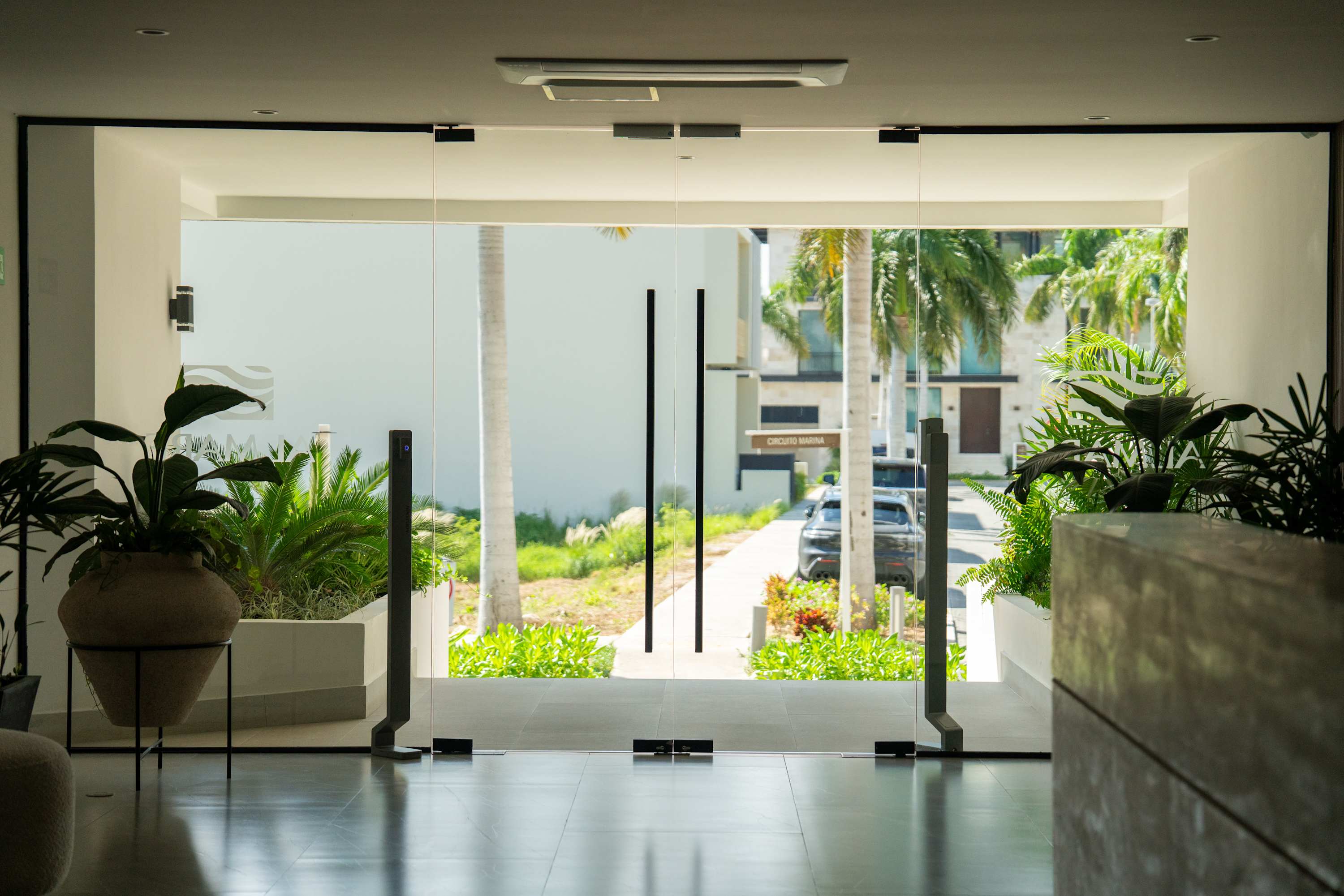 Modern glass entrance with plants and tropical landscaping.