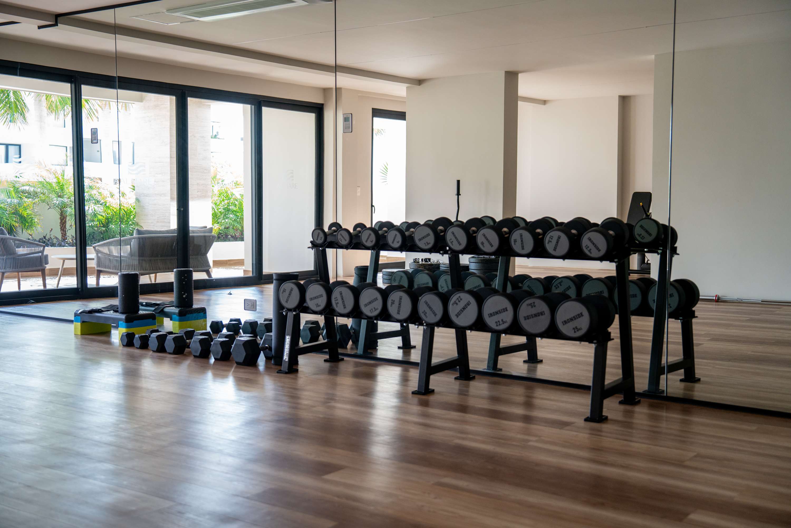 Dumbbell rack in a gym with mirrored walls and wooden floors.