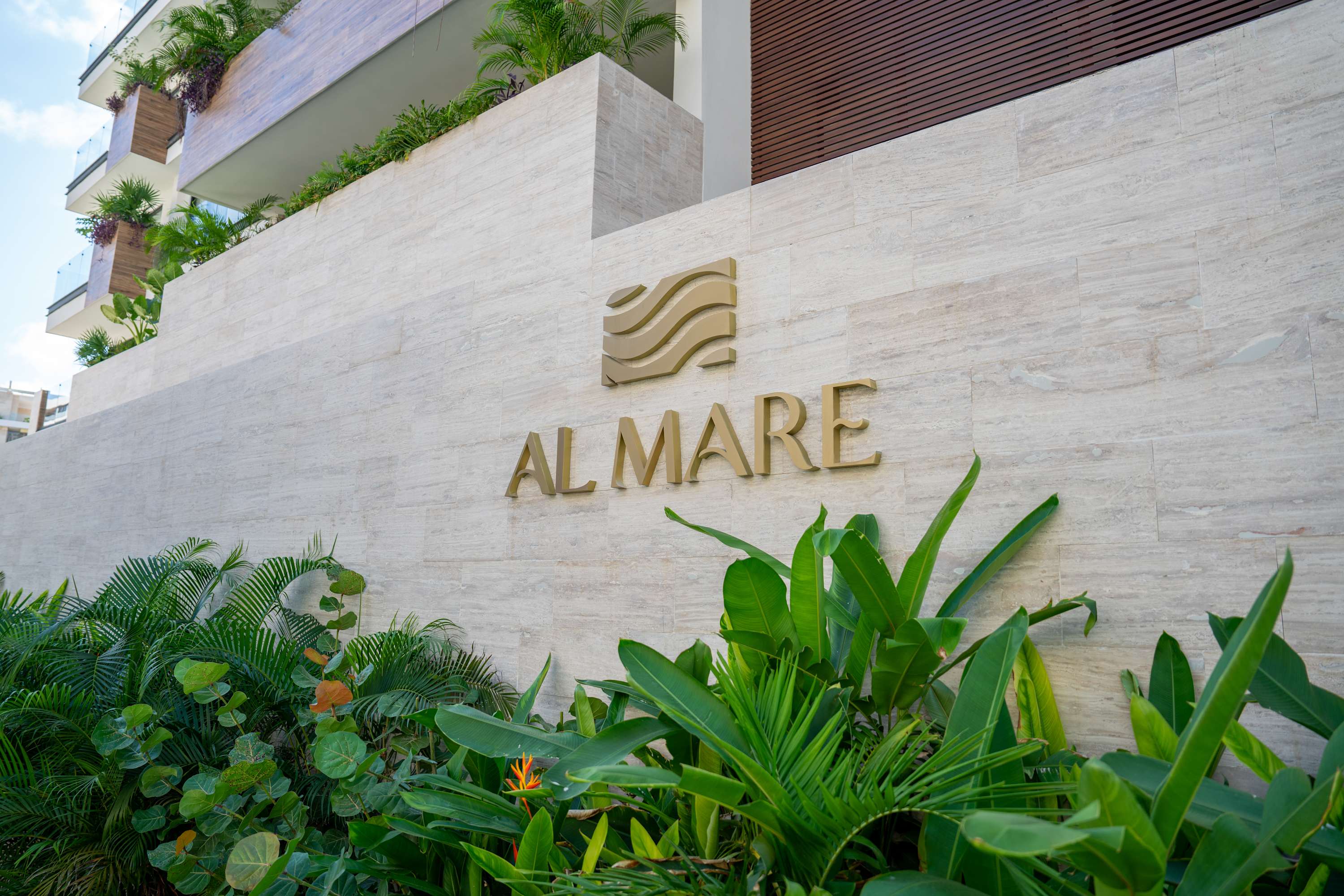 Sign for "AL MARE" residential building with tropical plants in front.