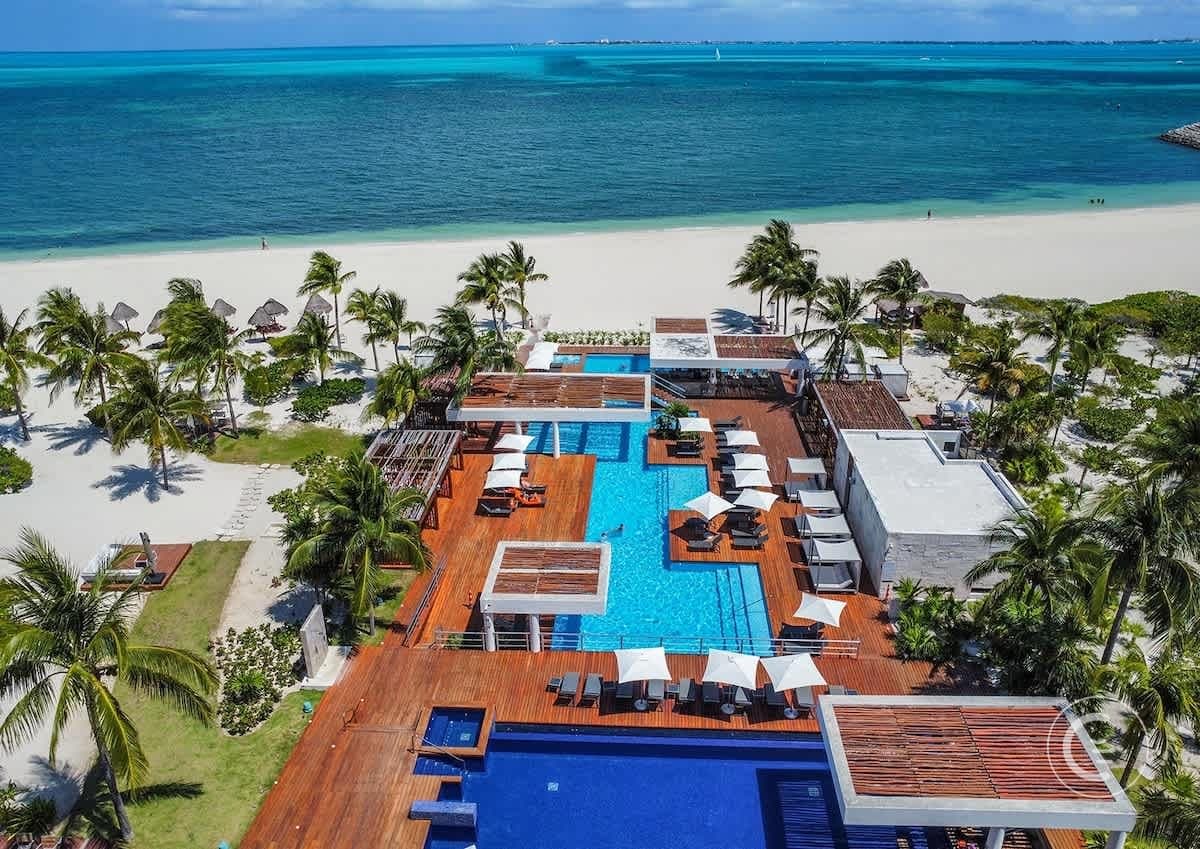 Tropical resort with infinity pools, palm trees, and a white sand beach on a sunny day.