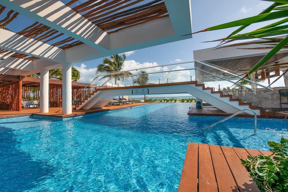 A stunning pool area with a bridge, lounge chairs, and palm trees, overlooking a beach.