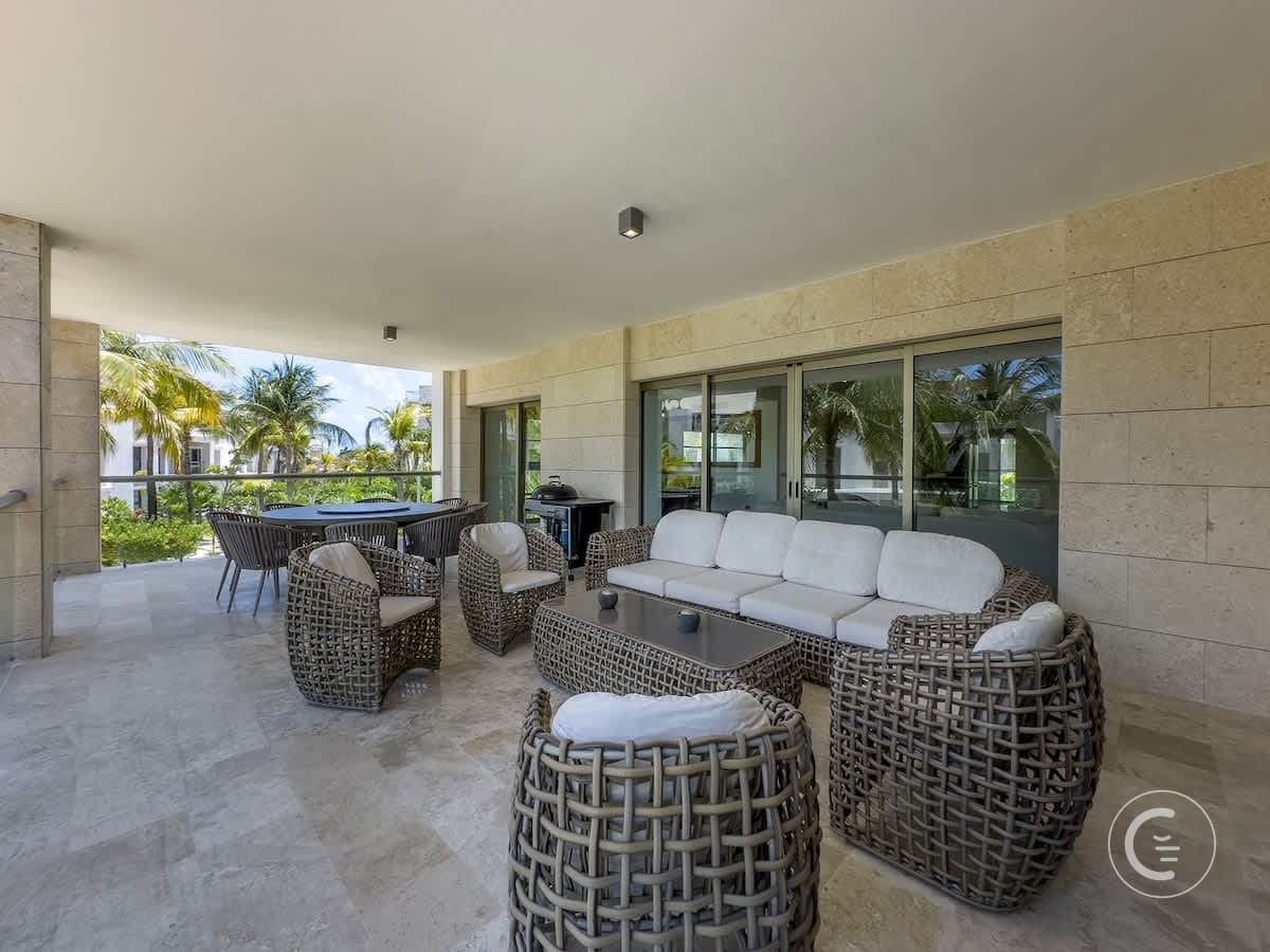 Spacious patio with wicker furniture, dining set, and view of palm trees and buildings.