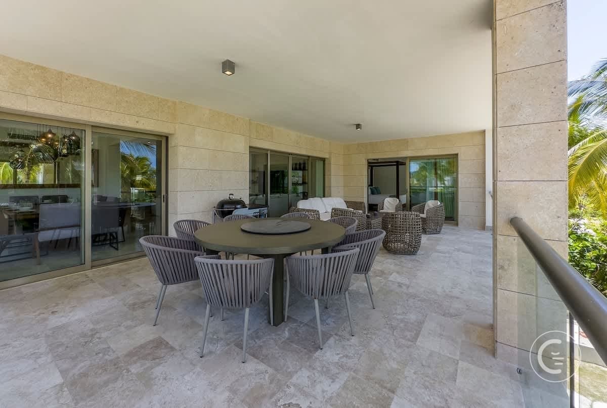 A patio with a round dining table and chairs, a grill, and wicker lounge chairs.