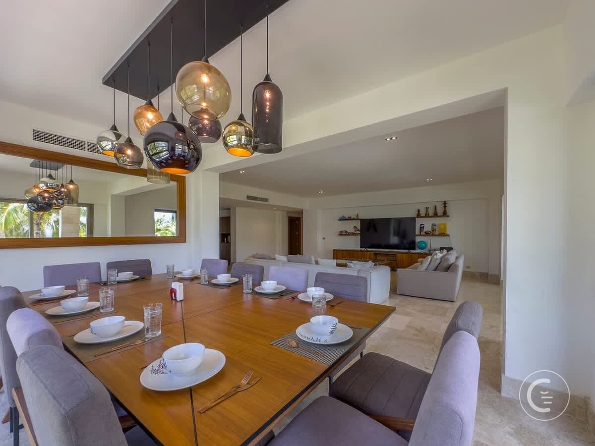 A modern dining room with a wooden table set for a meal, surrounded by plush chairs.