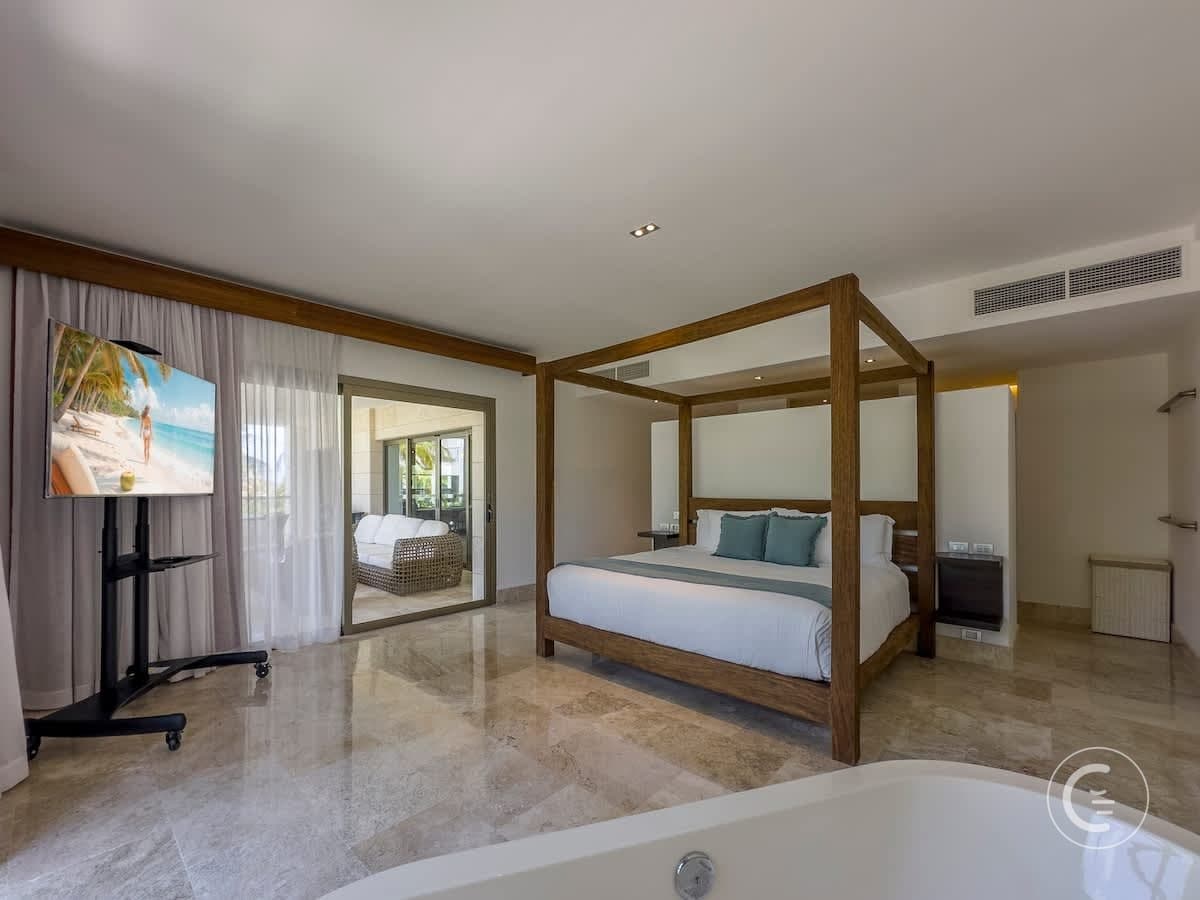 A modern bedroom with a four-poster bed, a large TV, and a bathtub.