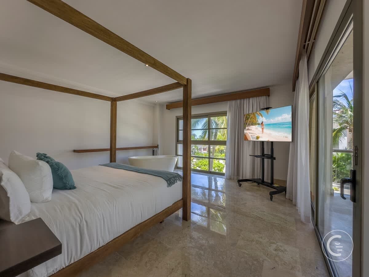 A bedroom with a four-poster bed, bathtub, and a TV displaying a beach scene.
