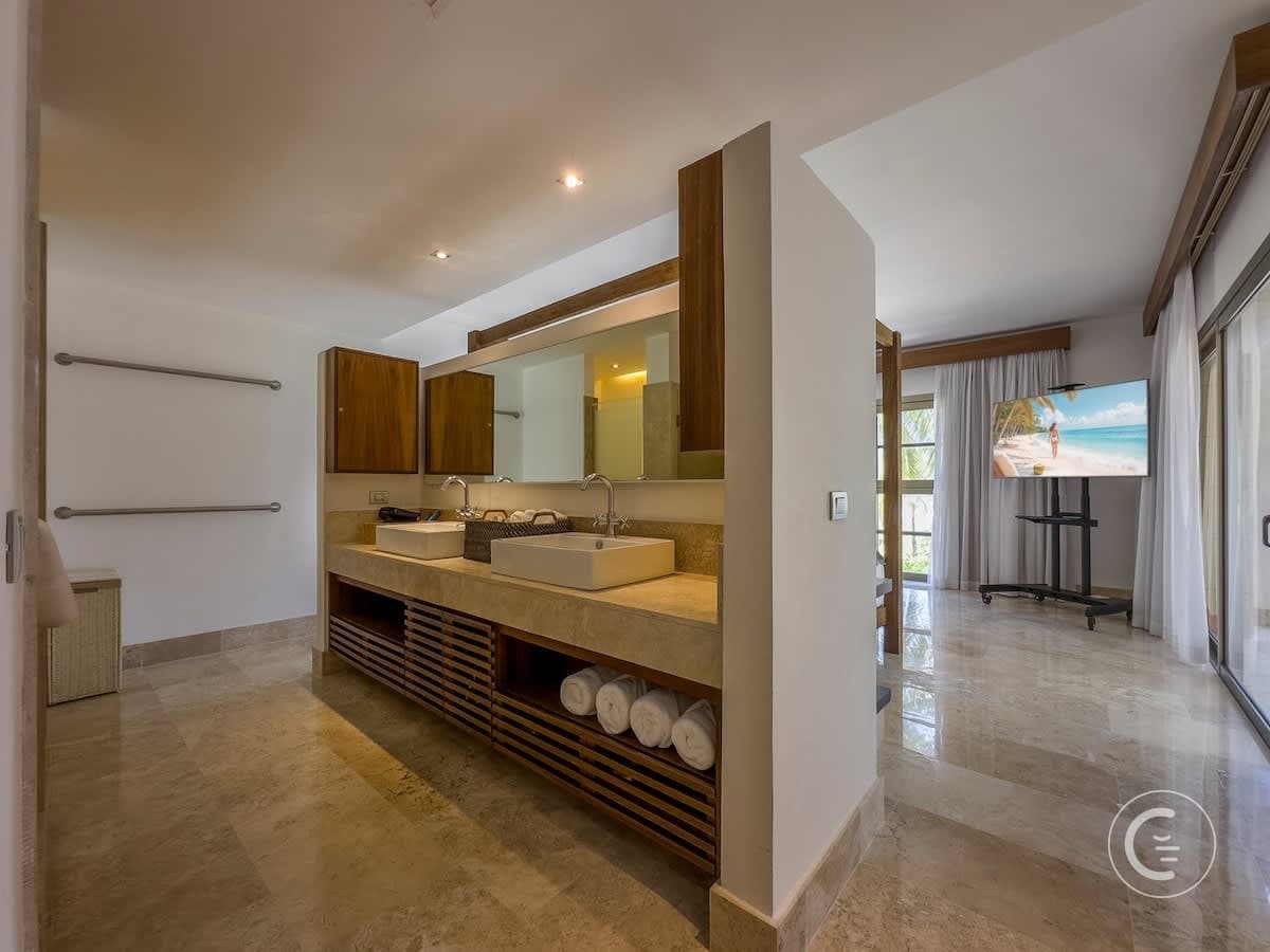 Modern bathroom with double sinks, wooden cabinets, and a TV.