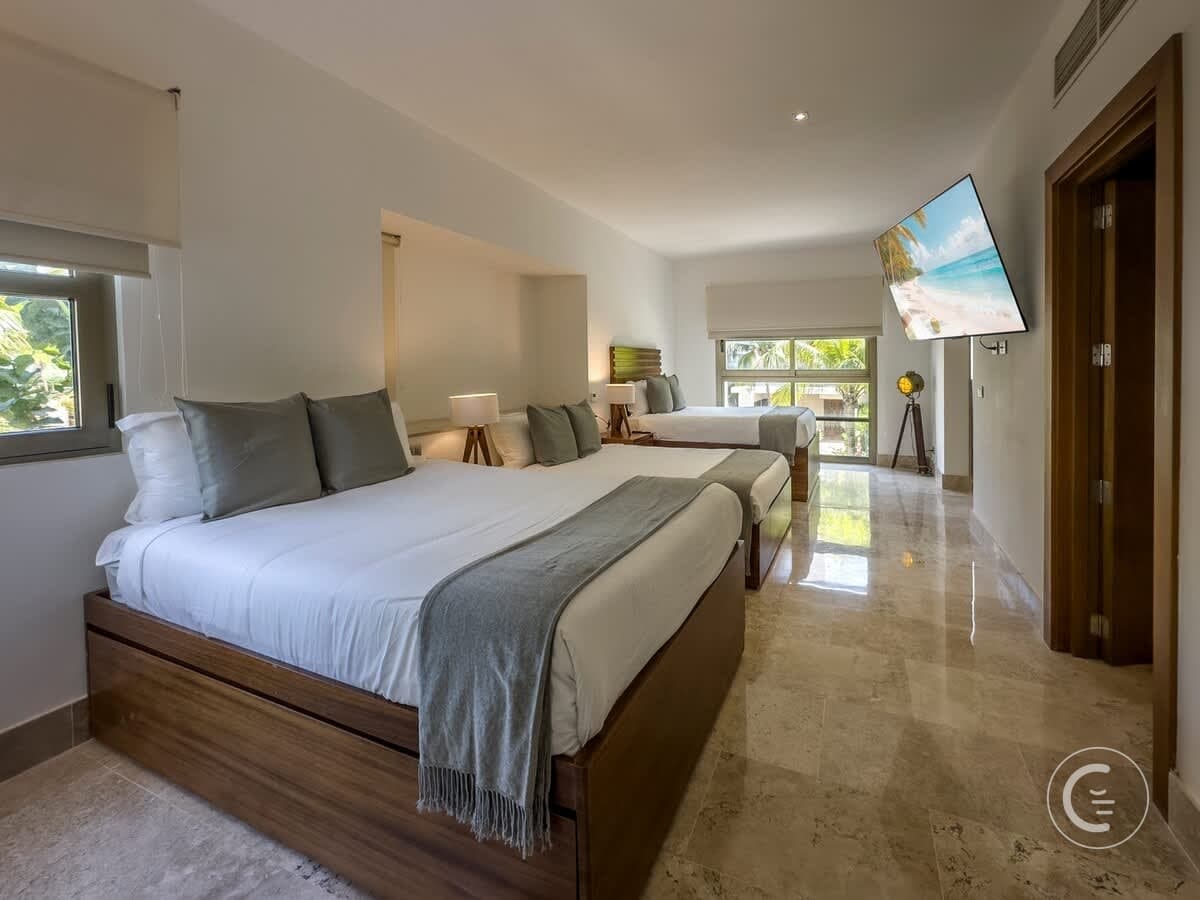 A hotel room with two queen beds, a TV, and a window view of palm trees.