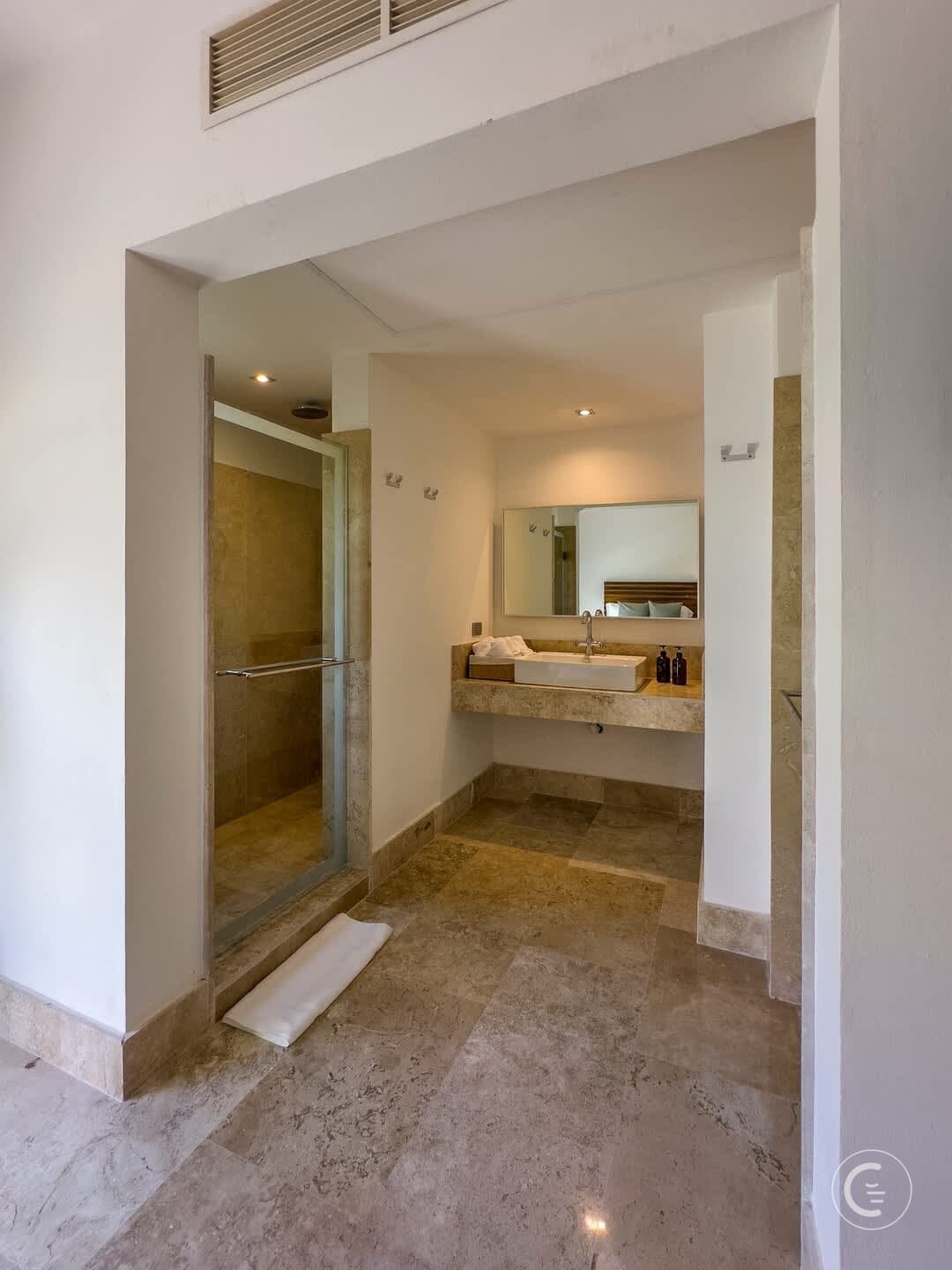 A modern bathroom with a glass-enclosed shower, a sink, and tiled floors.