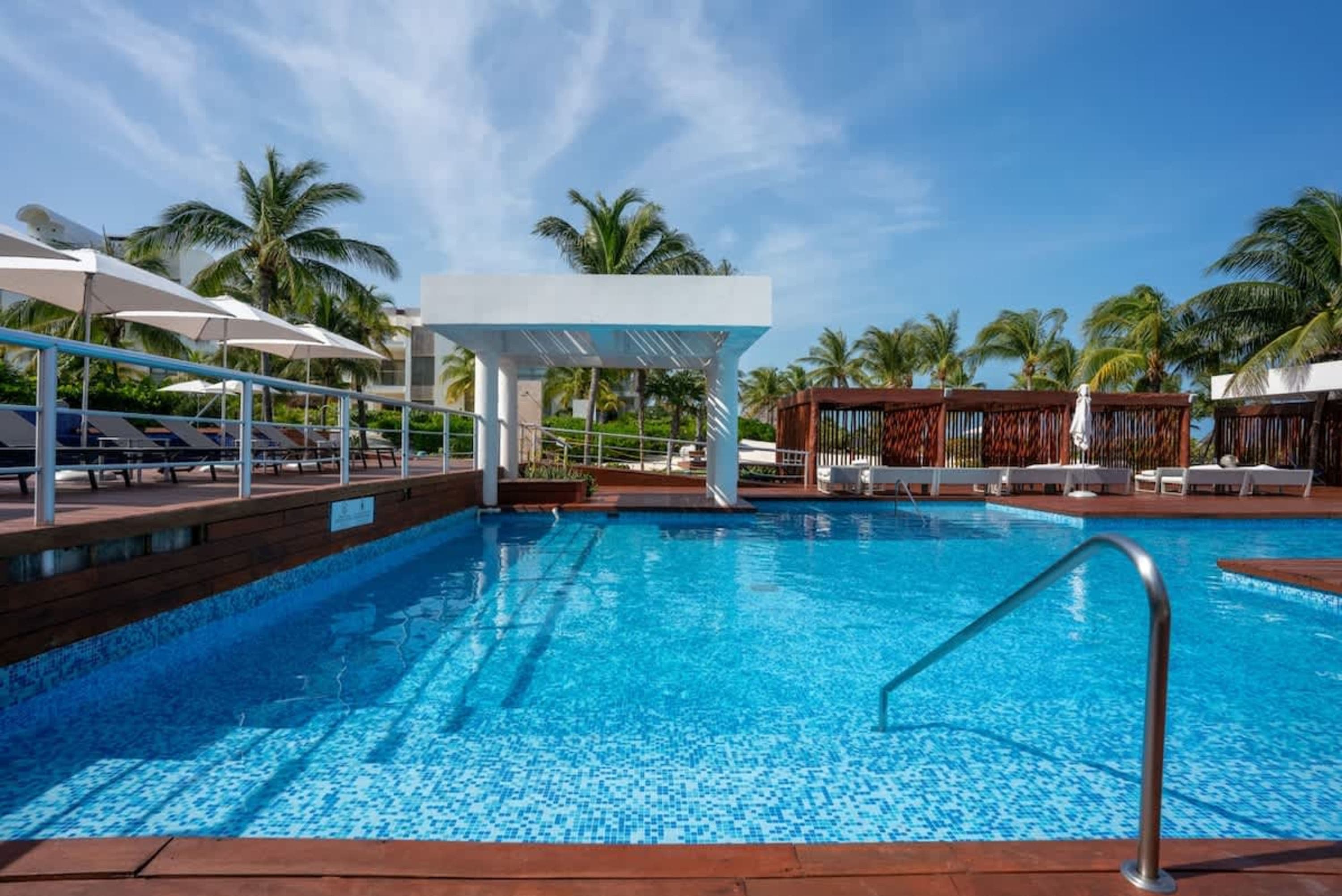 A bright blue swimming pool with lounge chairs and palm trees under a clear blue sky.