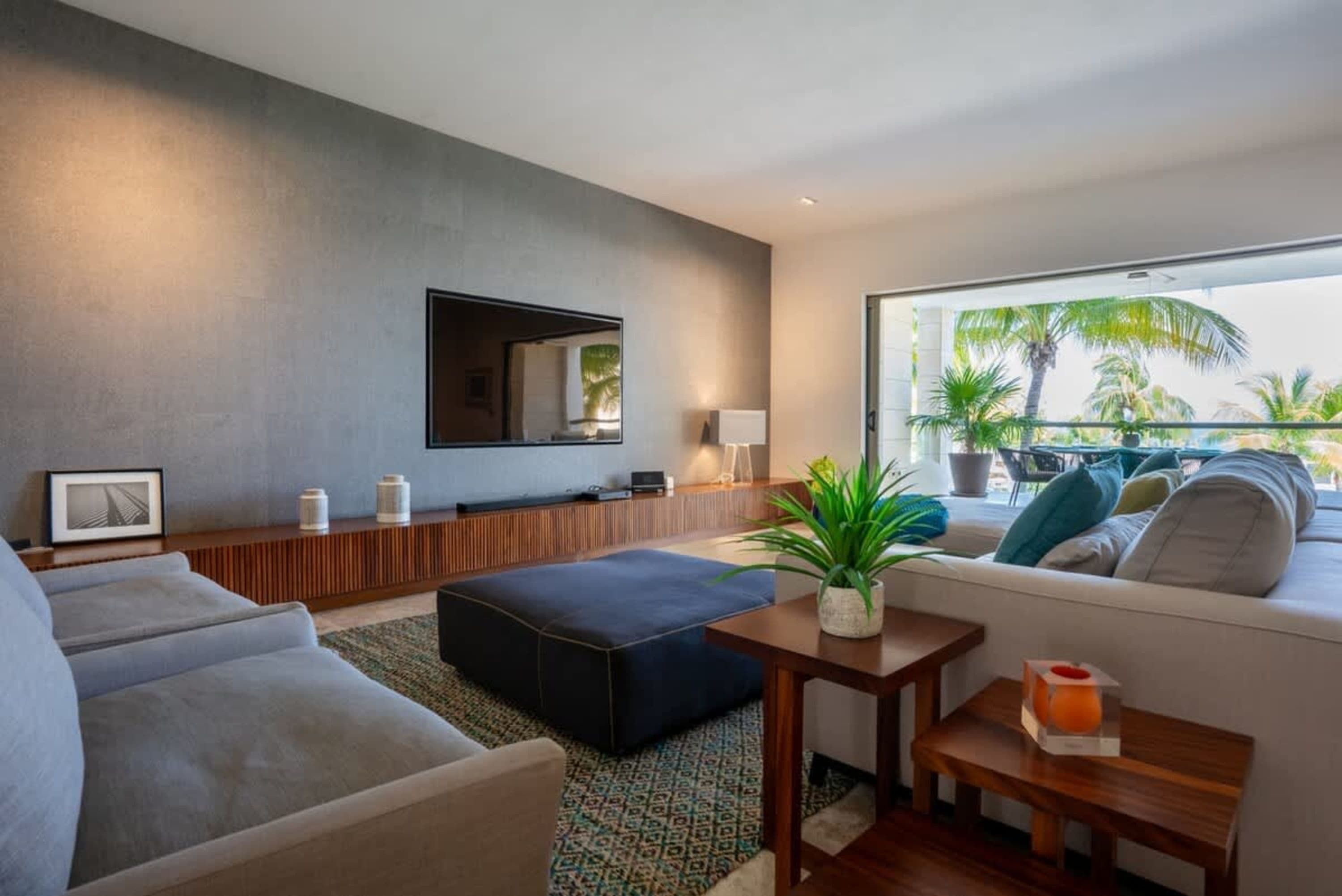 Living room with a gray textured wall, a TV, and a plush sofa with a view of palm trees.