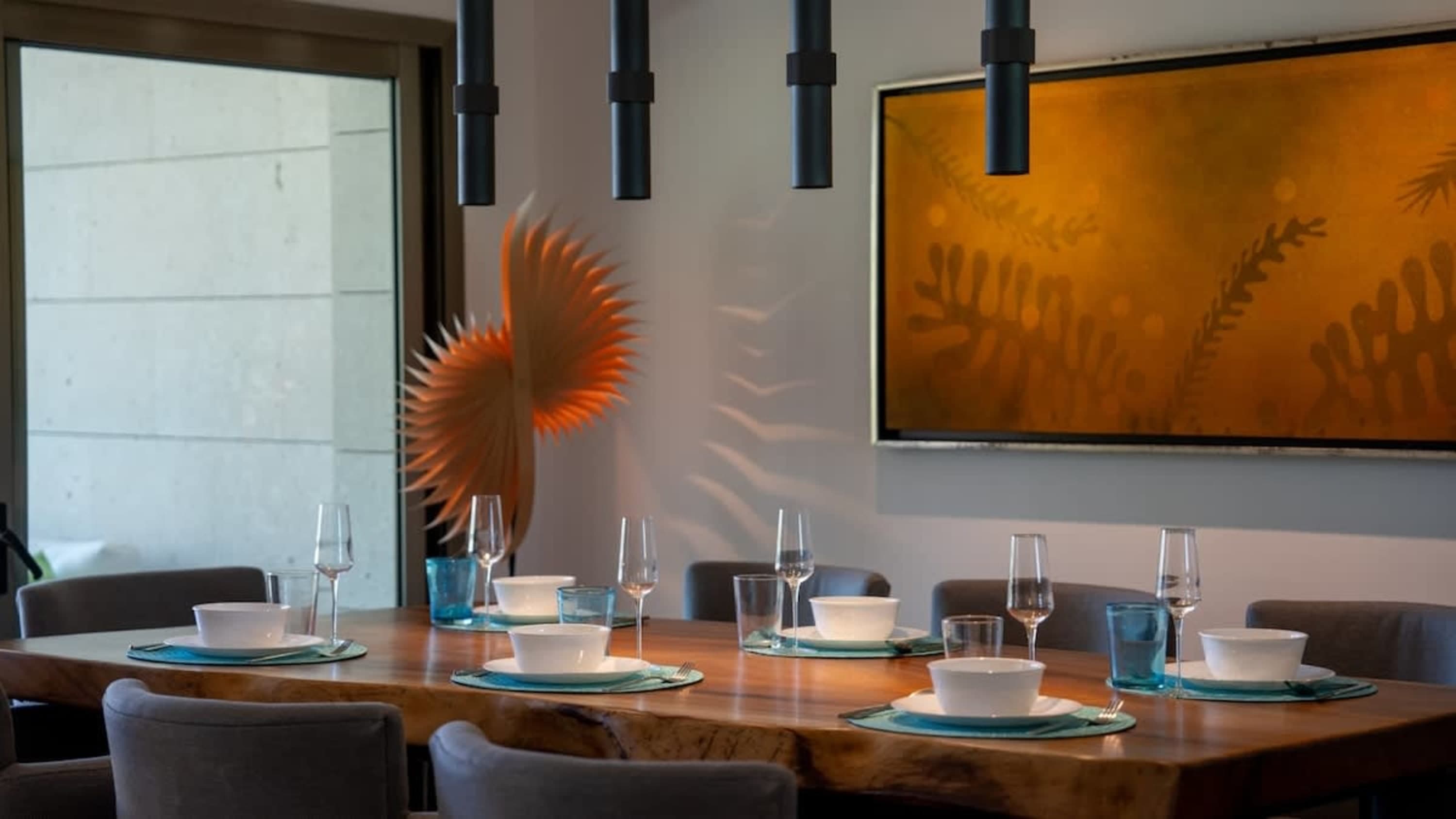 A dining table is set with white bowls, glasses, and blue placemats.