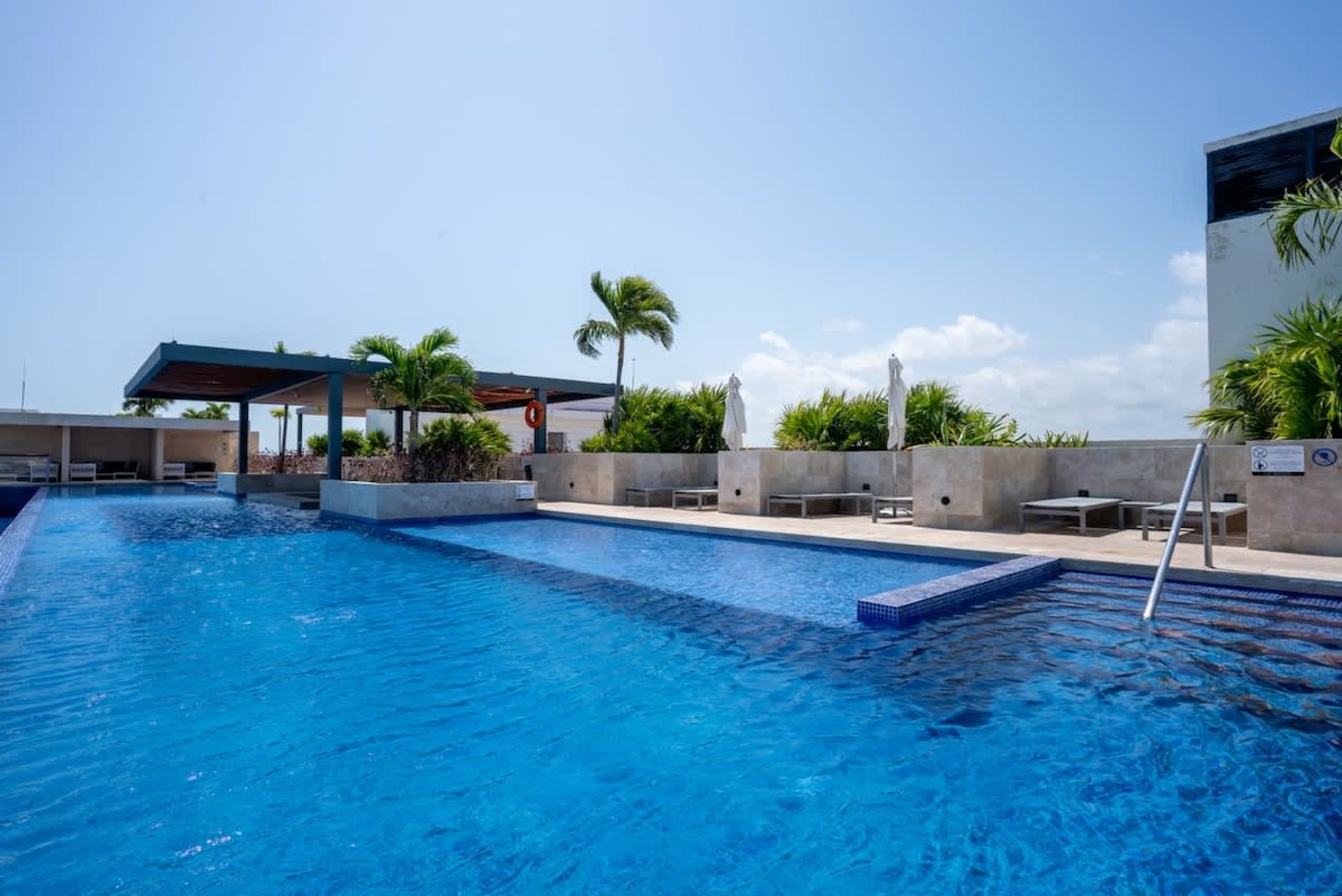 A bright blue swimming pool with lounge chairs and palm trees under a clear sky.
