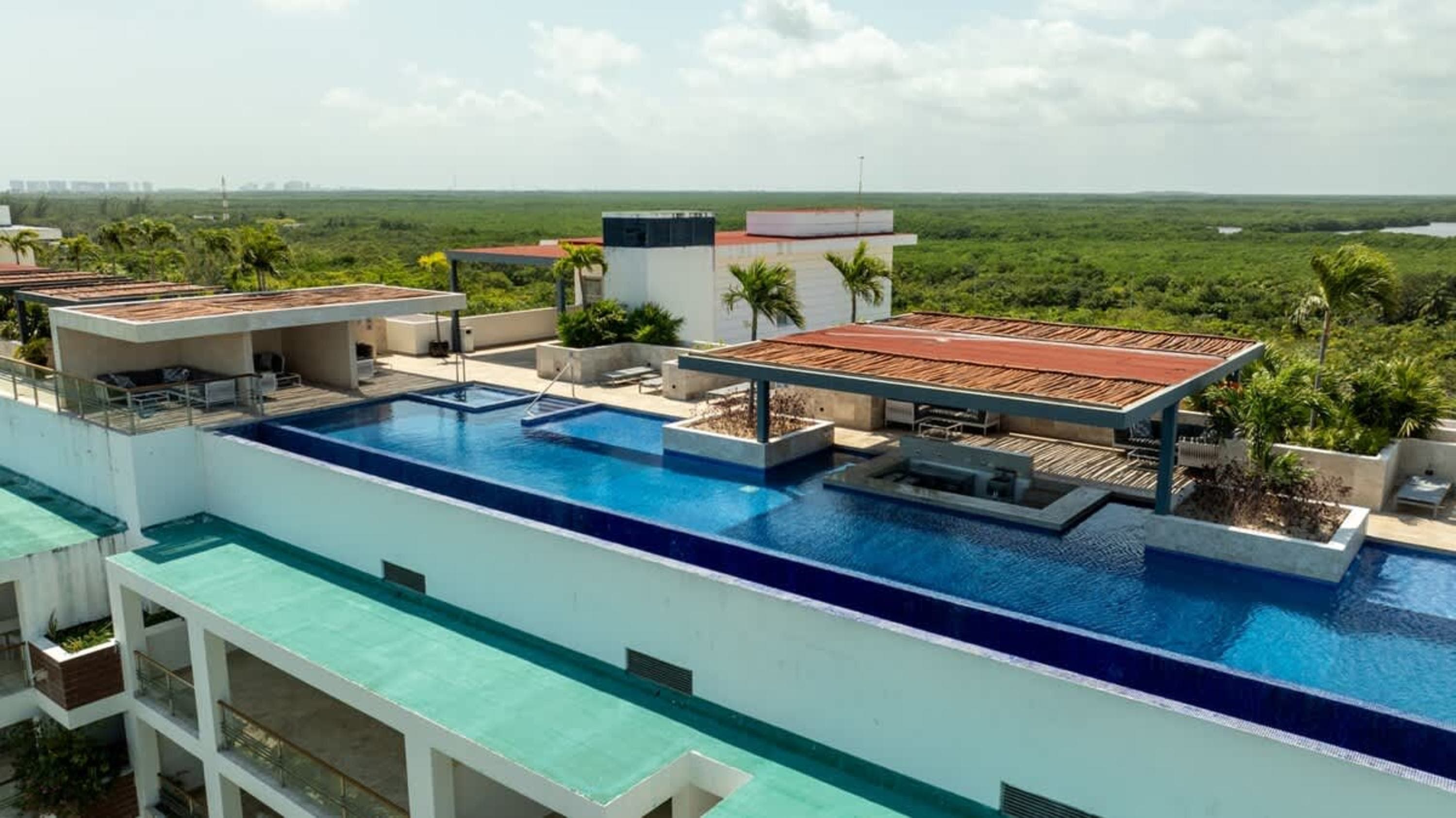 Rooftop swimming pool and lounge area overlooking lush green landscape and distant city skyline.