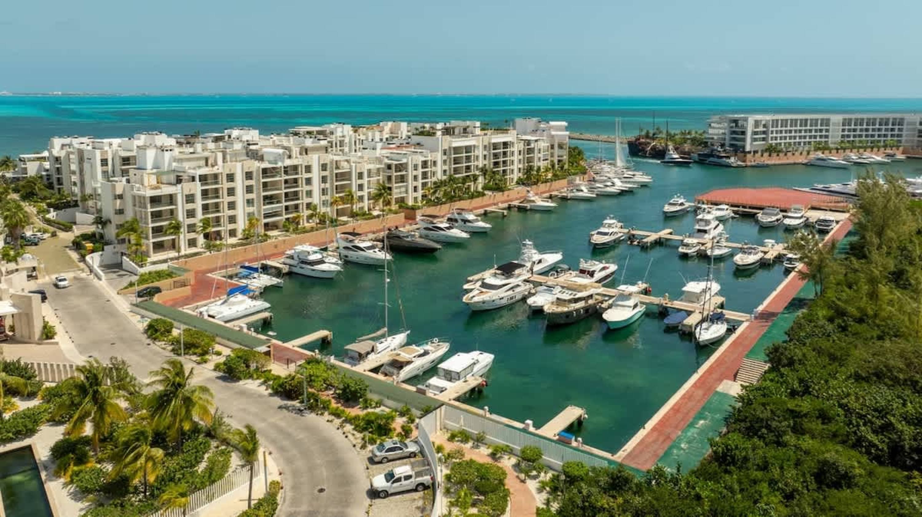 Luxury yachts and modern apartments line a clear turquoise harbor.