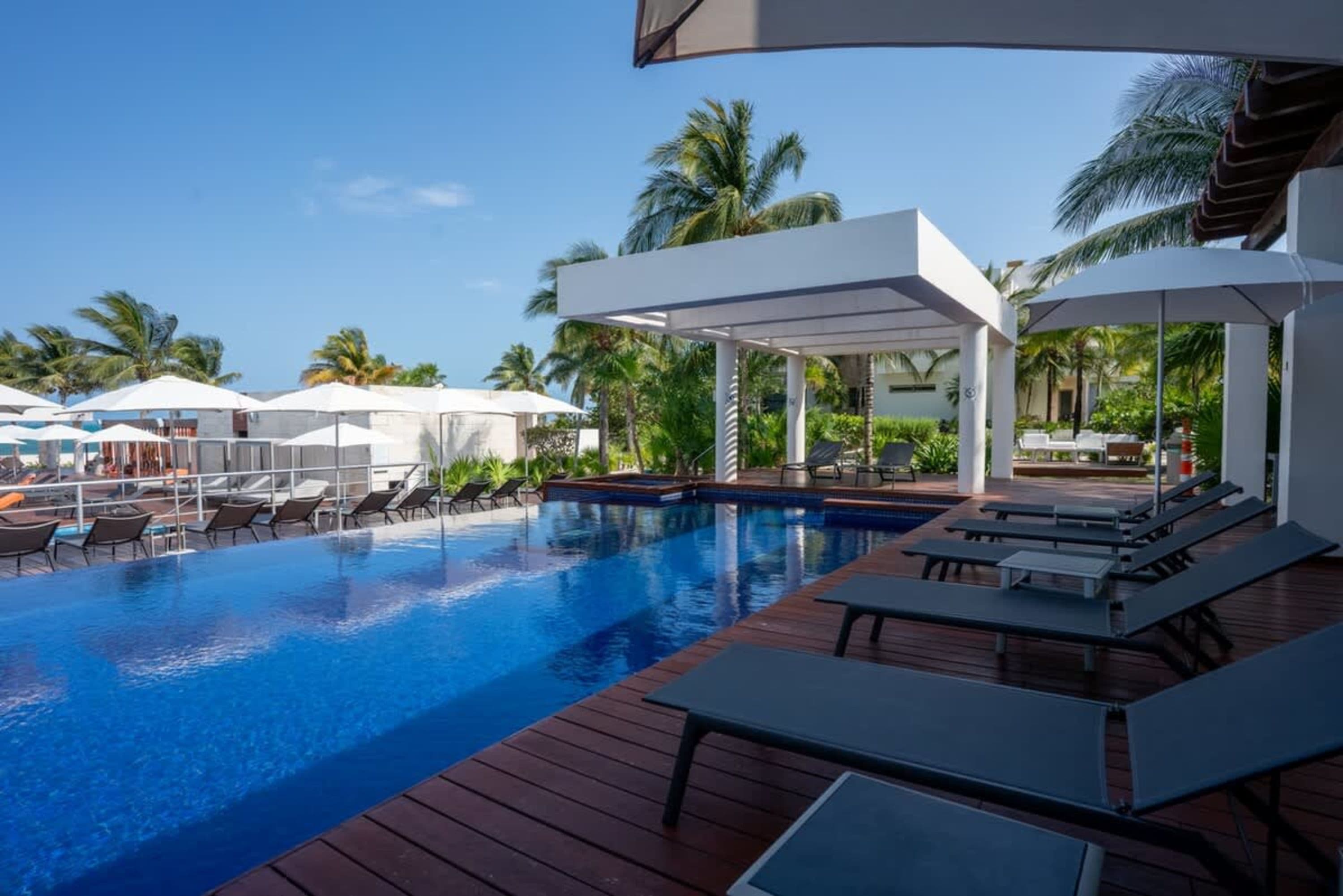 A beautiful resort pool area with lounge chairs and palm trees under a clear blue sky.
