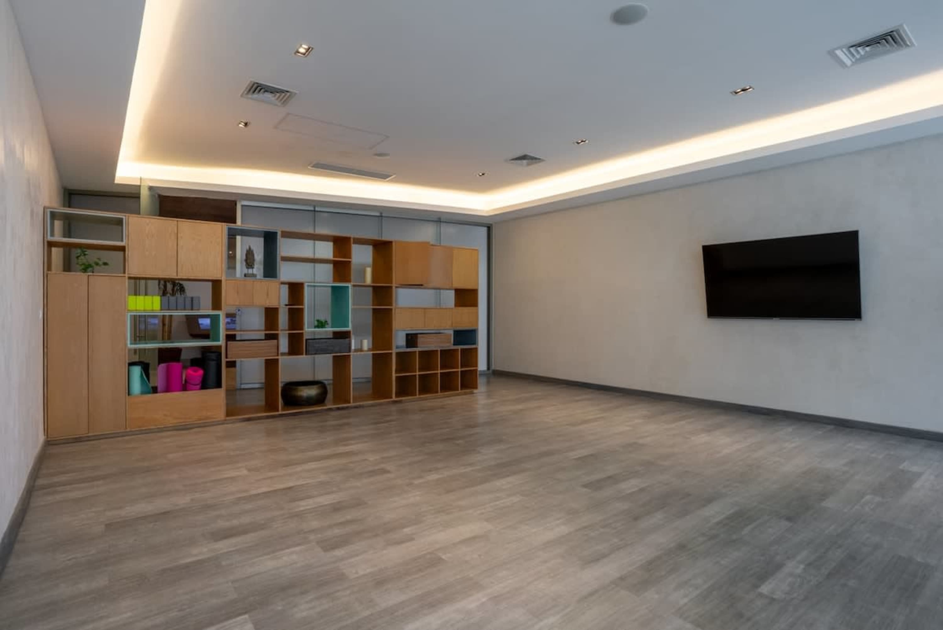 A large, empty room with a modern wooden bookshelf on the left and a TV on the right wall.