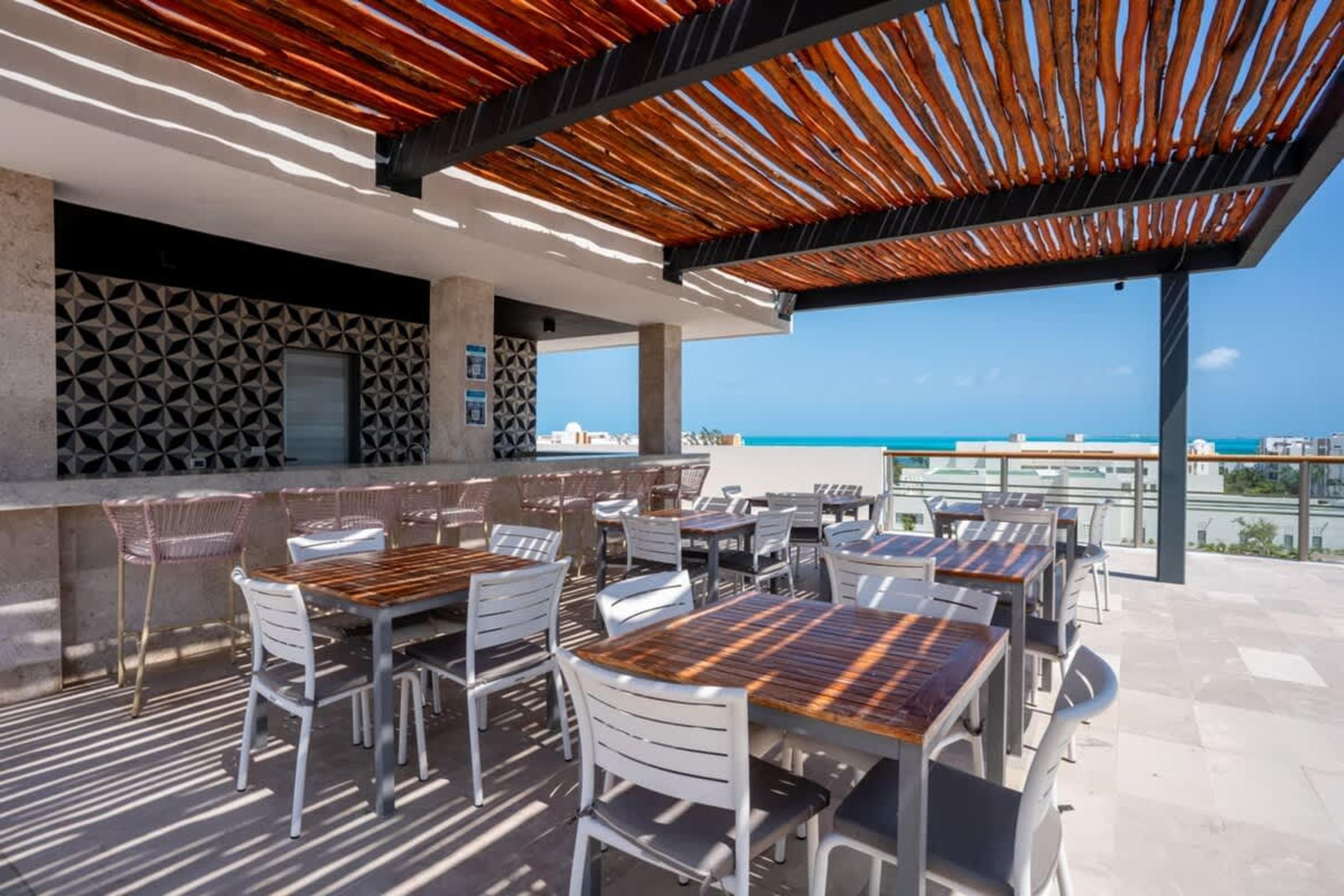Rooftop bar with tables and chairs overlooking the ocean.