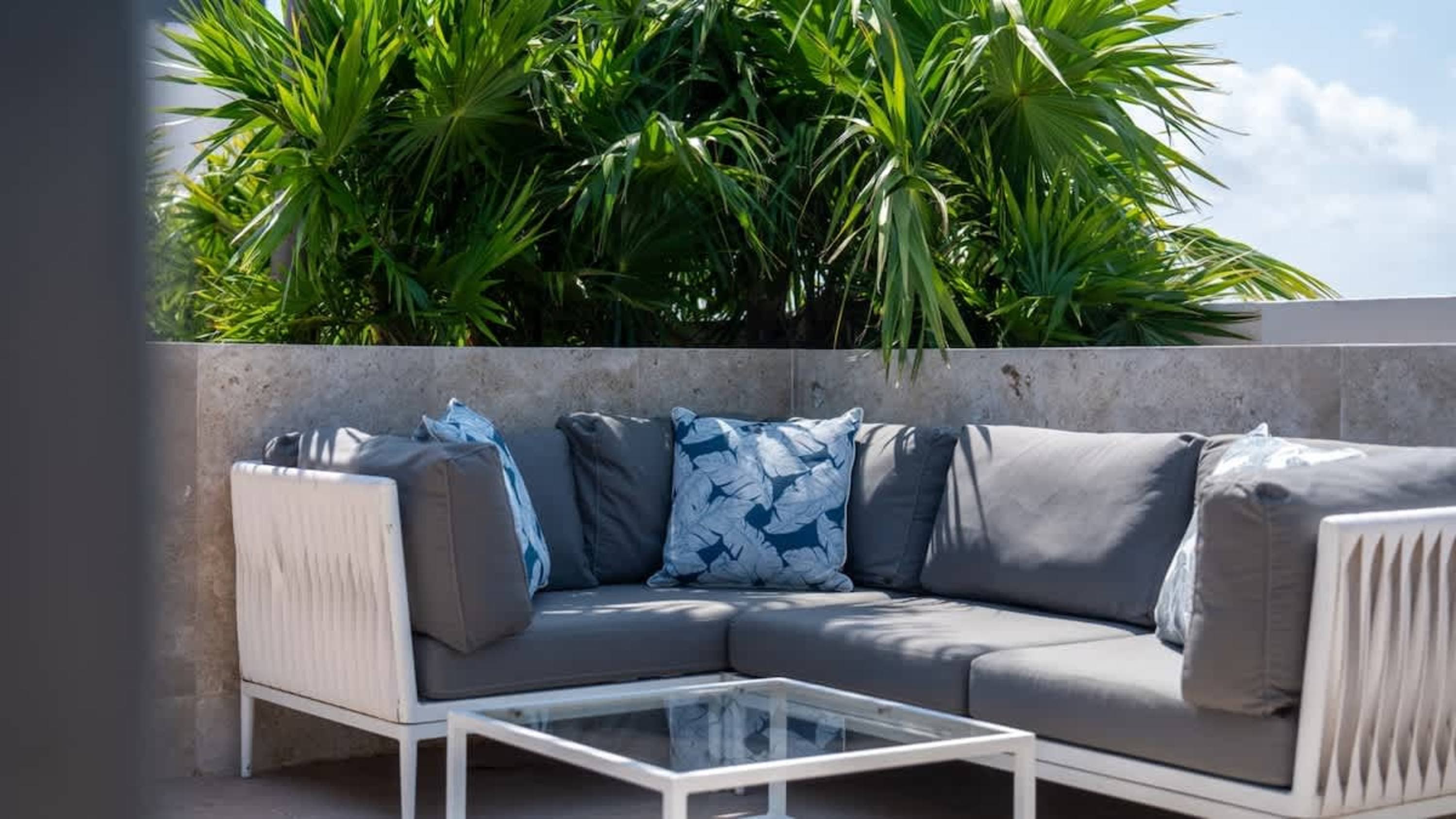 An outdoor sectional sofa with gray cushions and white framed arms sits on a patio.