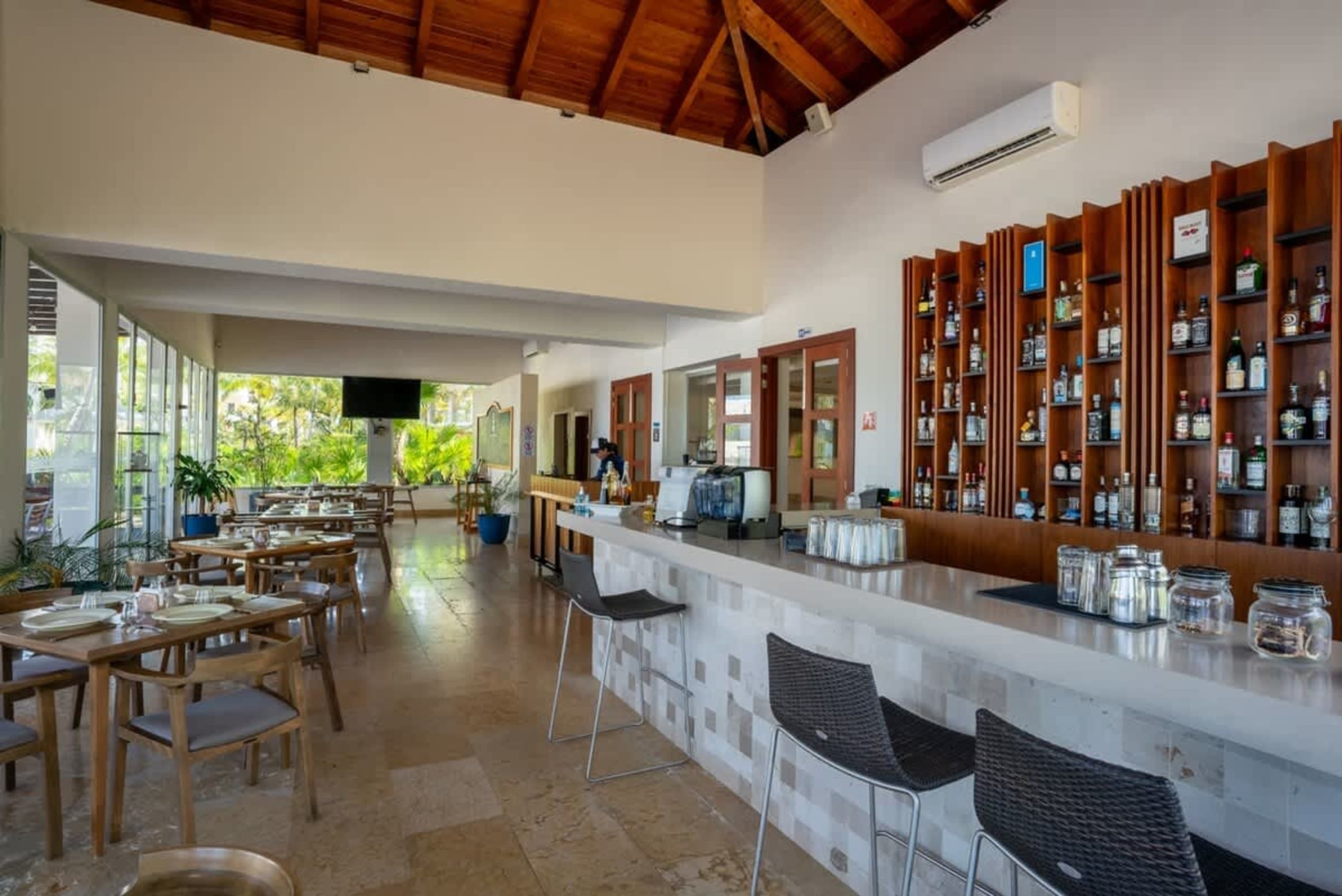 An indoor restaurant with a bar, tables, and chairs, featuring a wooden ceiling.