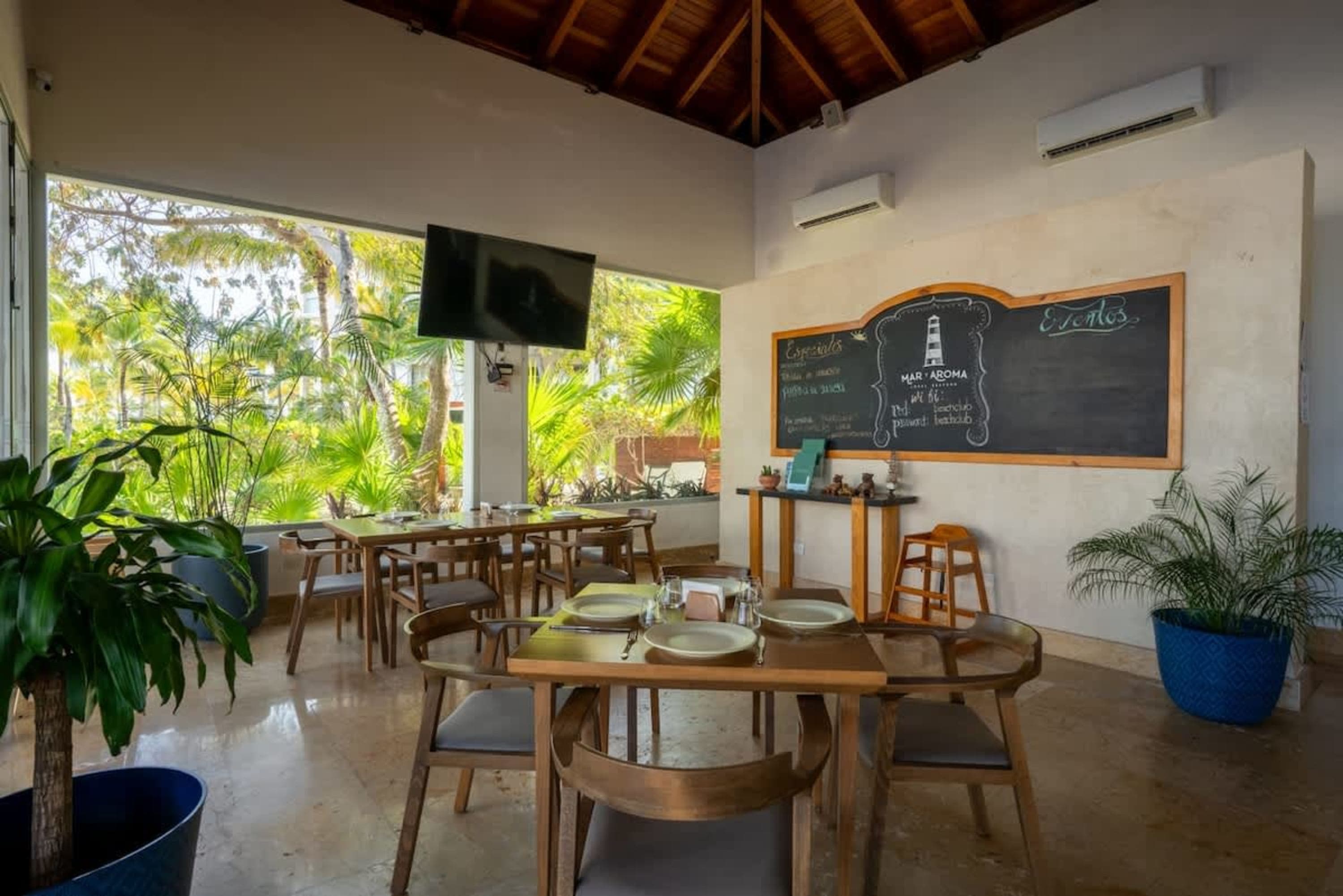 Dining tables and chairs with a view of lush greenery and a blackboard menu.