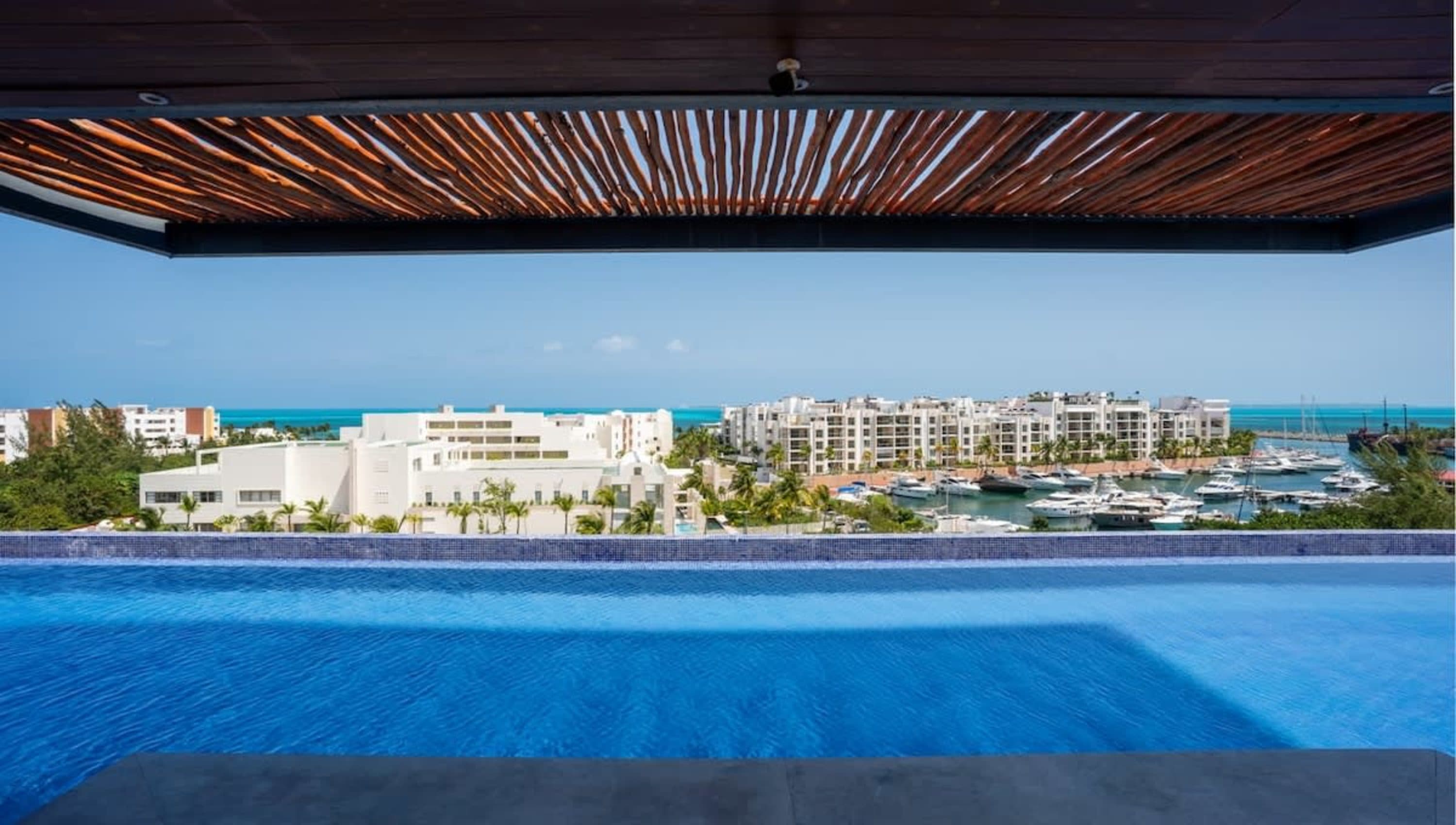 Infinity pool overlooking a marina filled with yachts and white buildings under a clear blue sky.