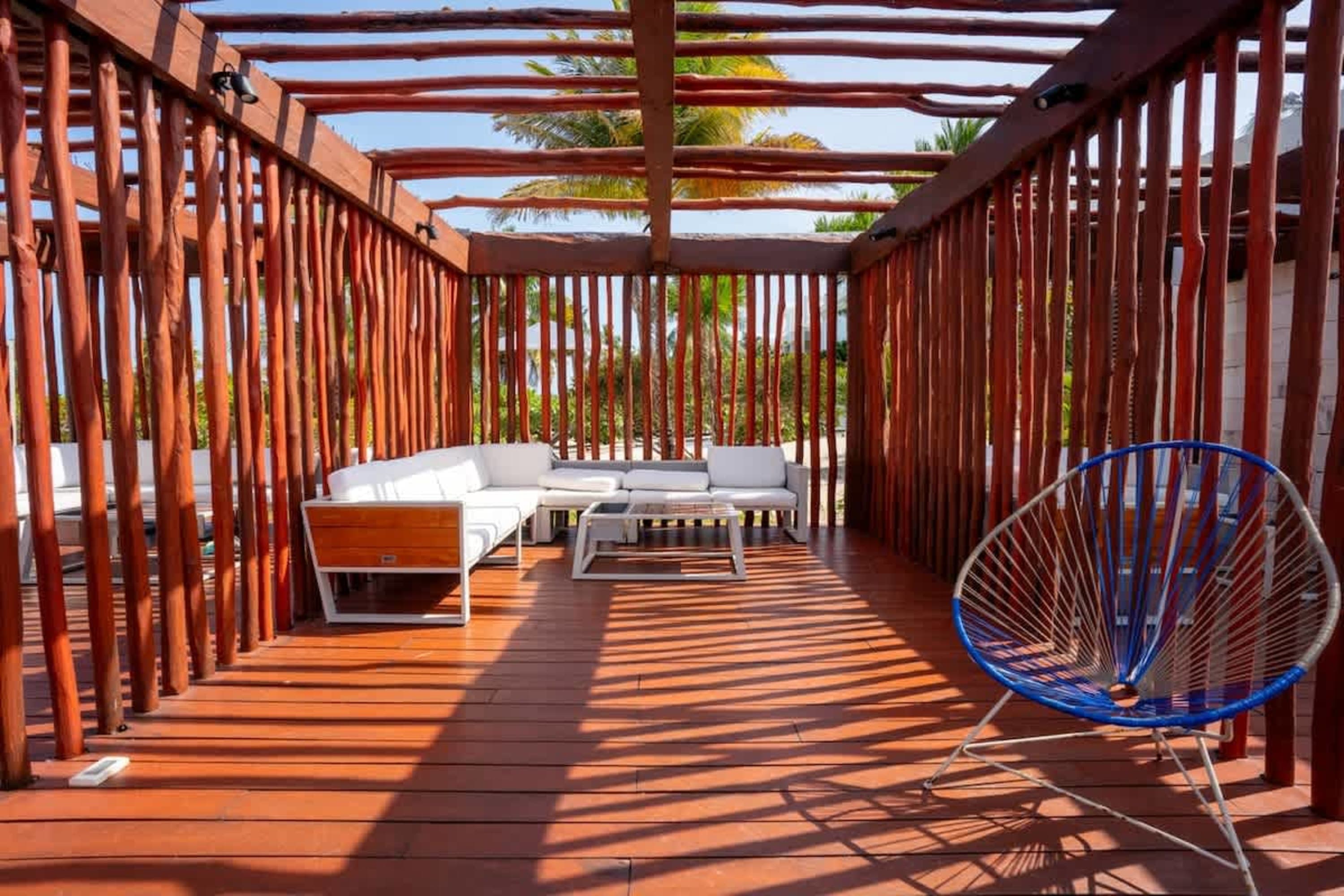 Outdoor seating area with a wooden pergola, white sectional sofa, and a colorful woven chair.