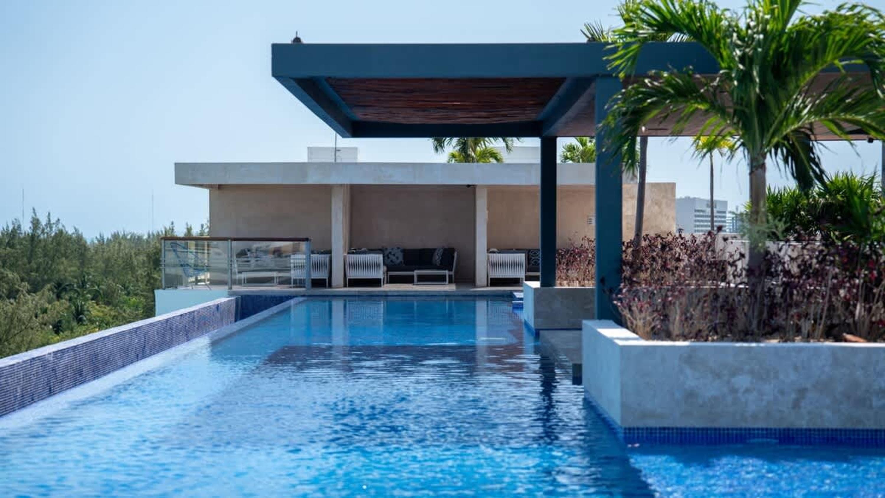 A luxury rooftop pool with palm trees, lounge seating, and a view of the ocean.