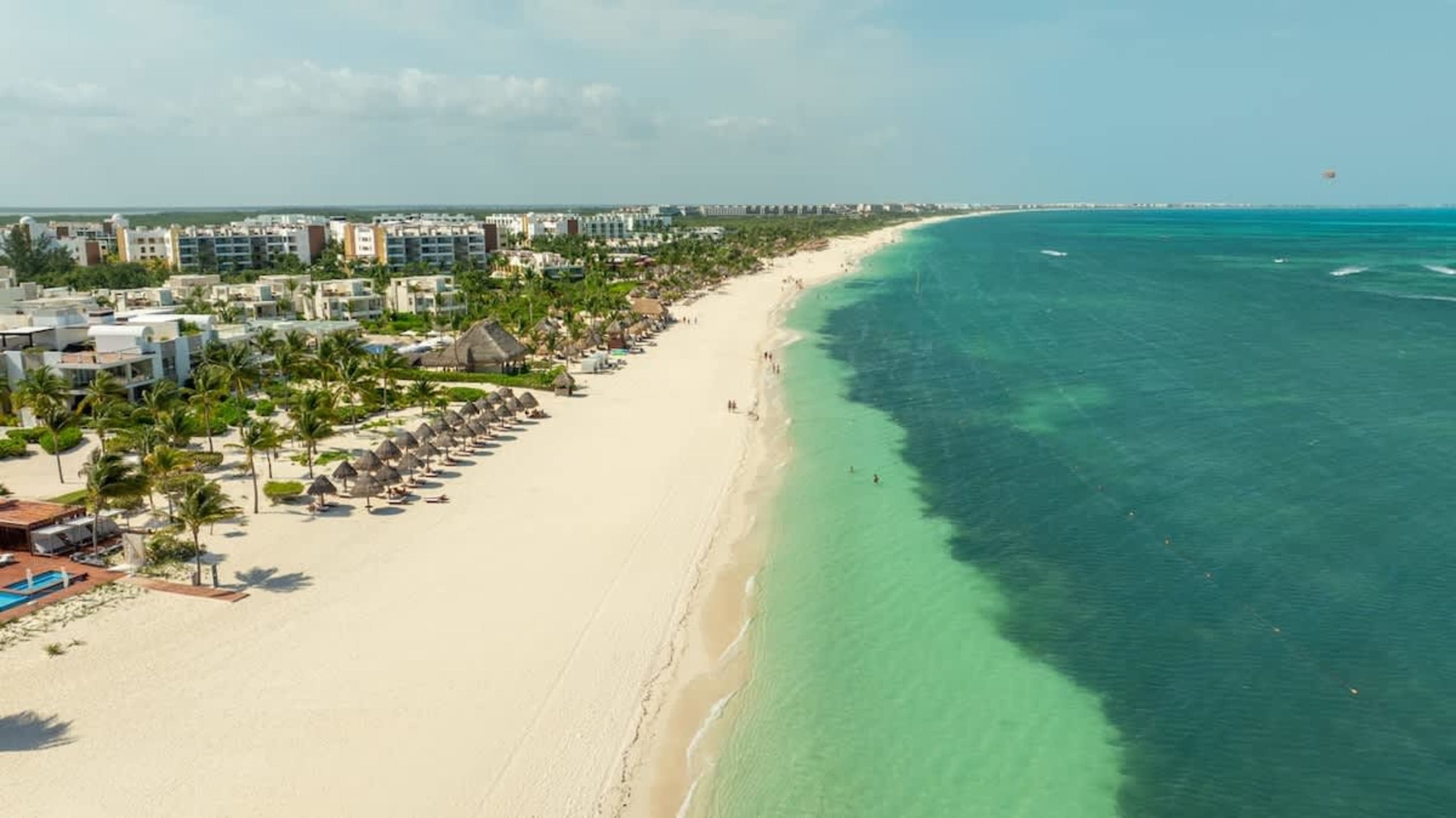 Resort hotels and thatched palapas line a white sand beach bordering the turquoise Caribbean Sea.