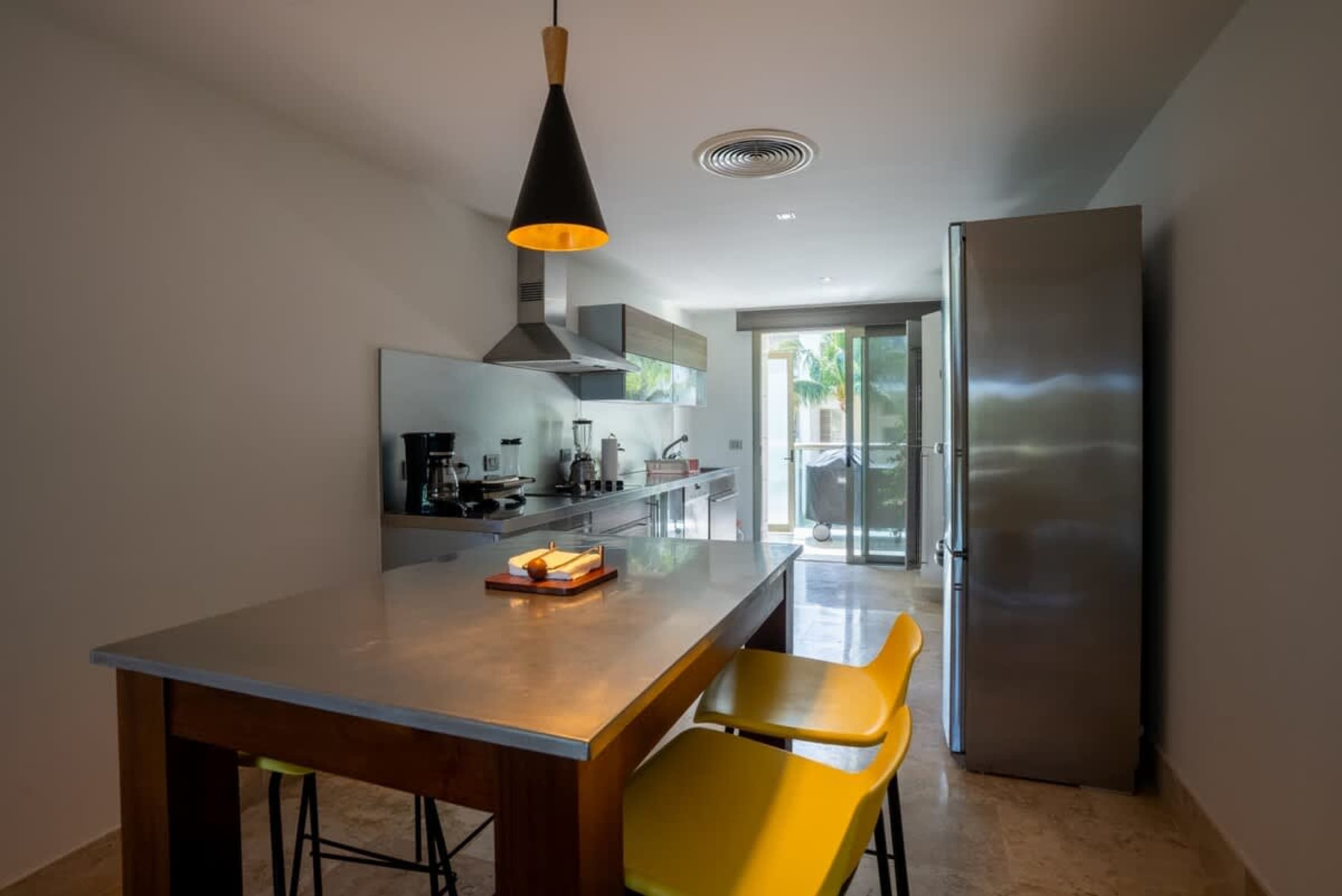 A modern kitchen with stainless steel appliances, a concrete island with yellow stools, and a glass 