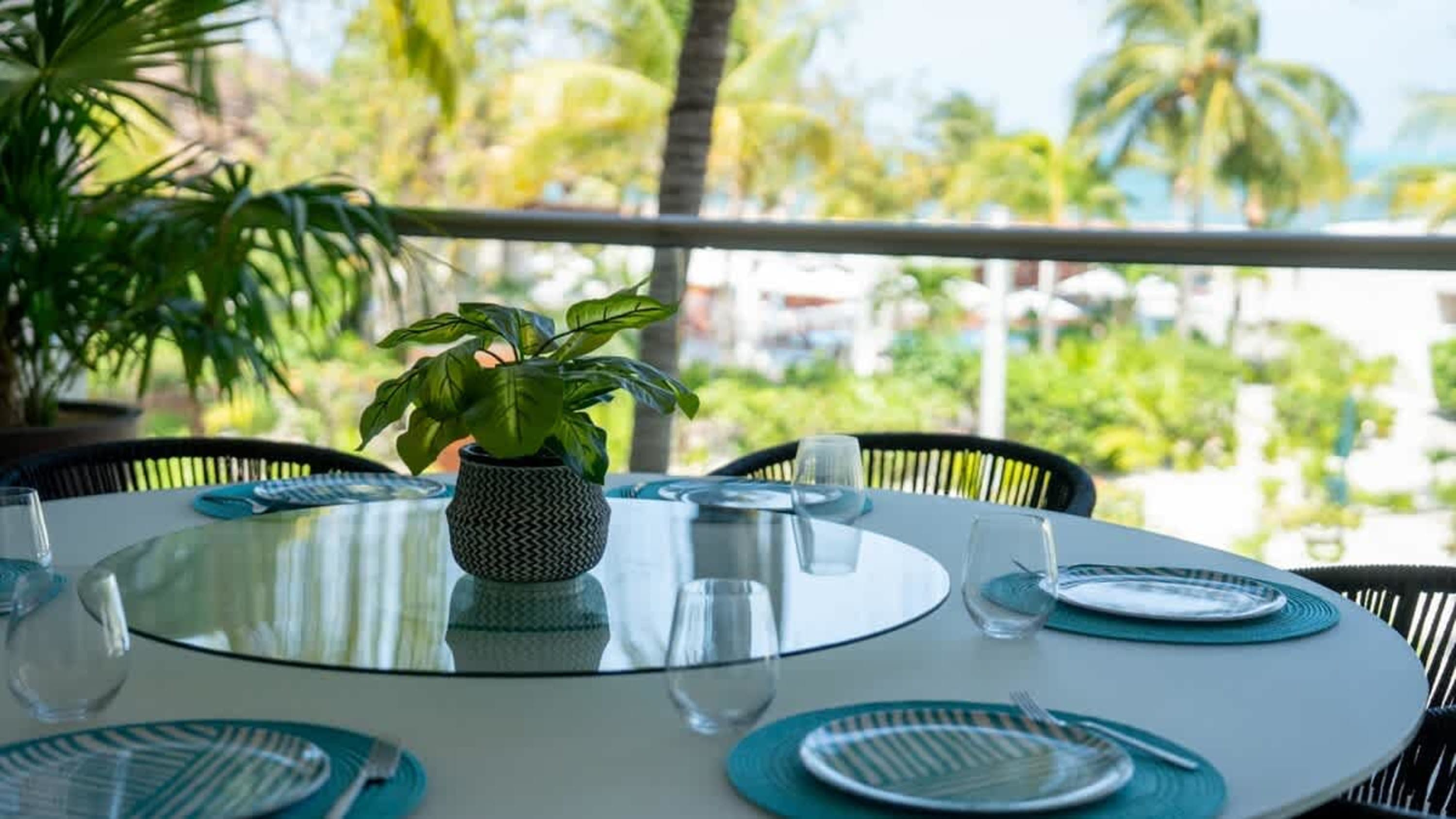 A round dining table is set for a meal with plates, glasses, and a plant.