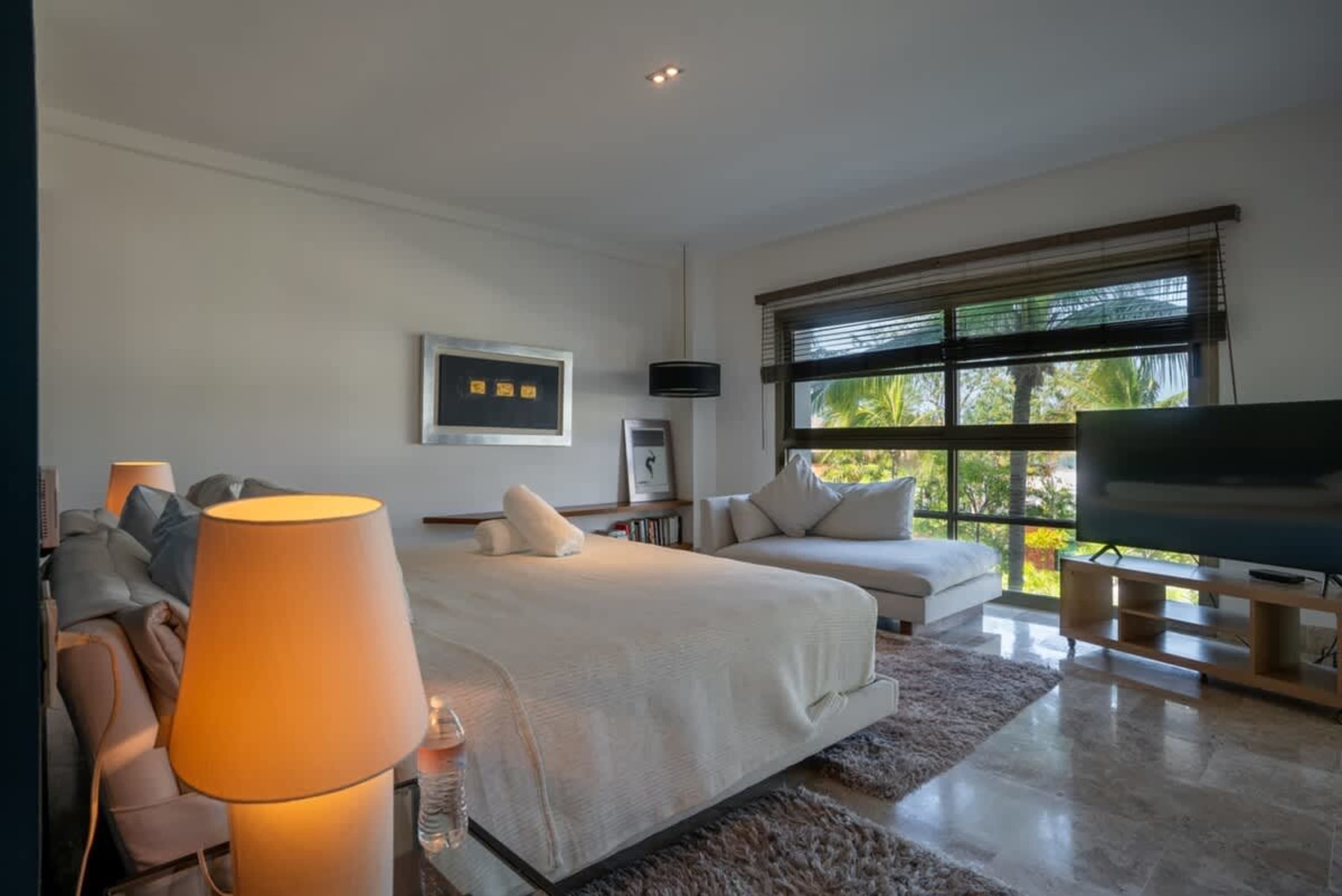 A spacious bedroom with a large bed, chaise lounge, and a TV.