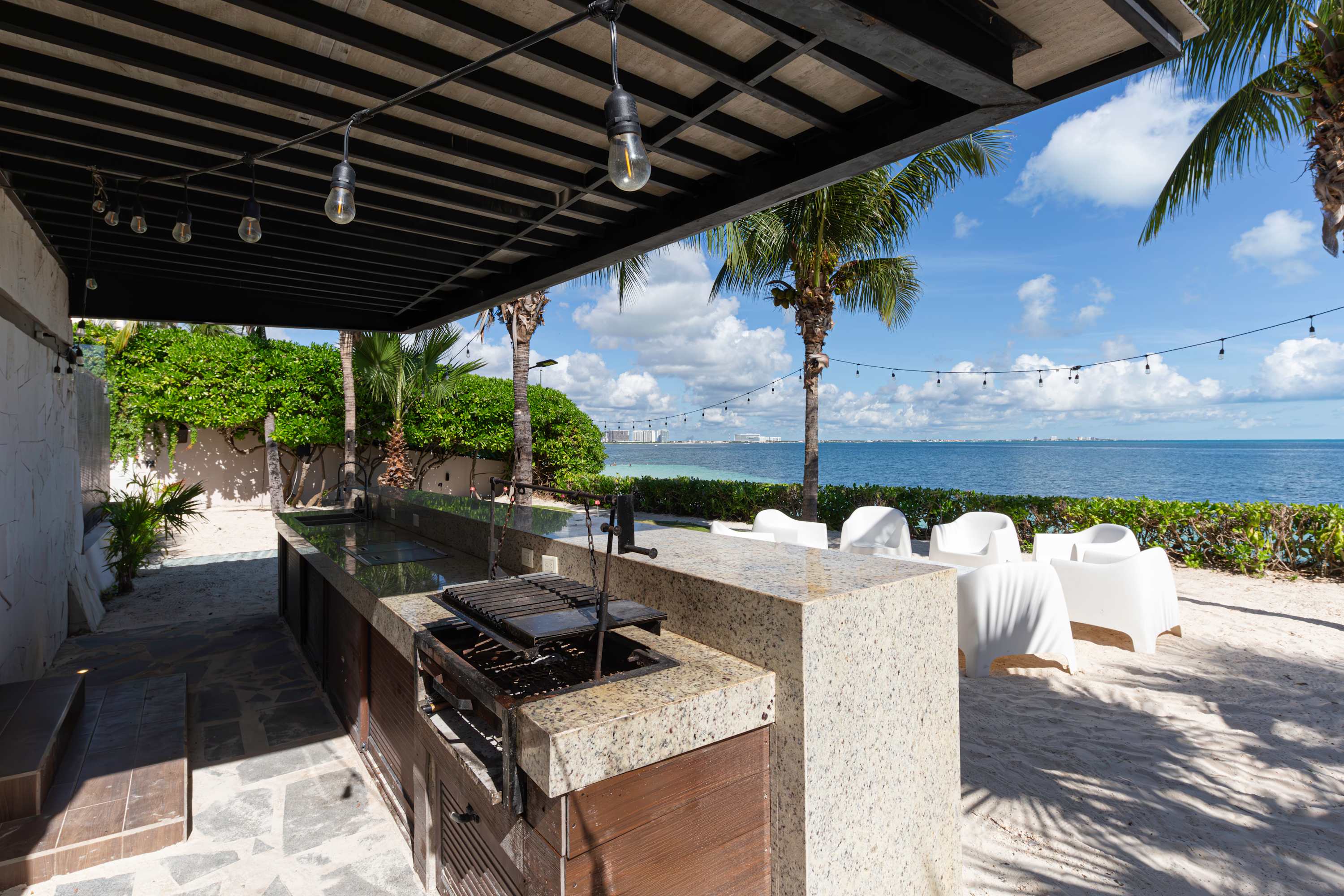 Outdoor kitchen with a grill and bar on a sandy beach overlooking the ocean.