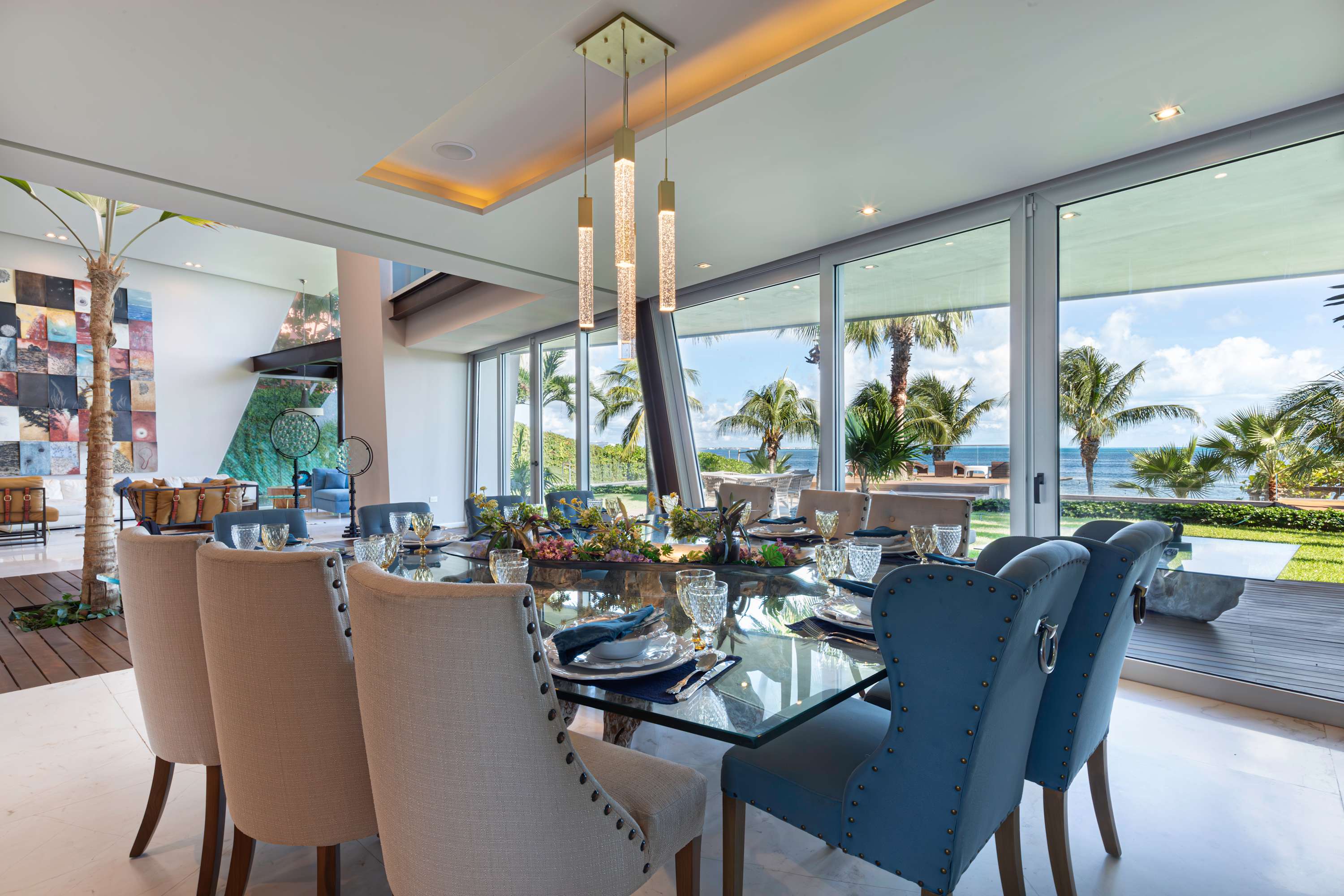 Luxury dining room with glass table, blue and tan chairs, and ocean view.