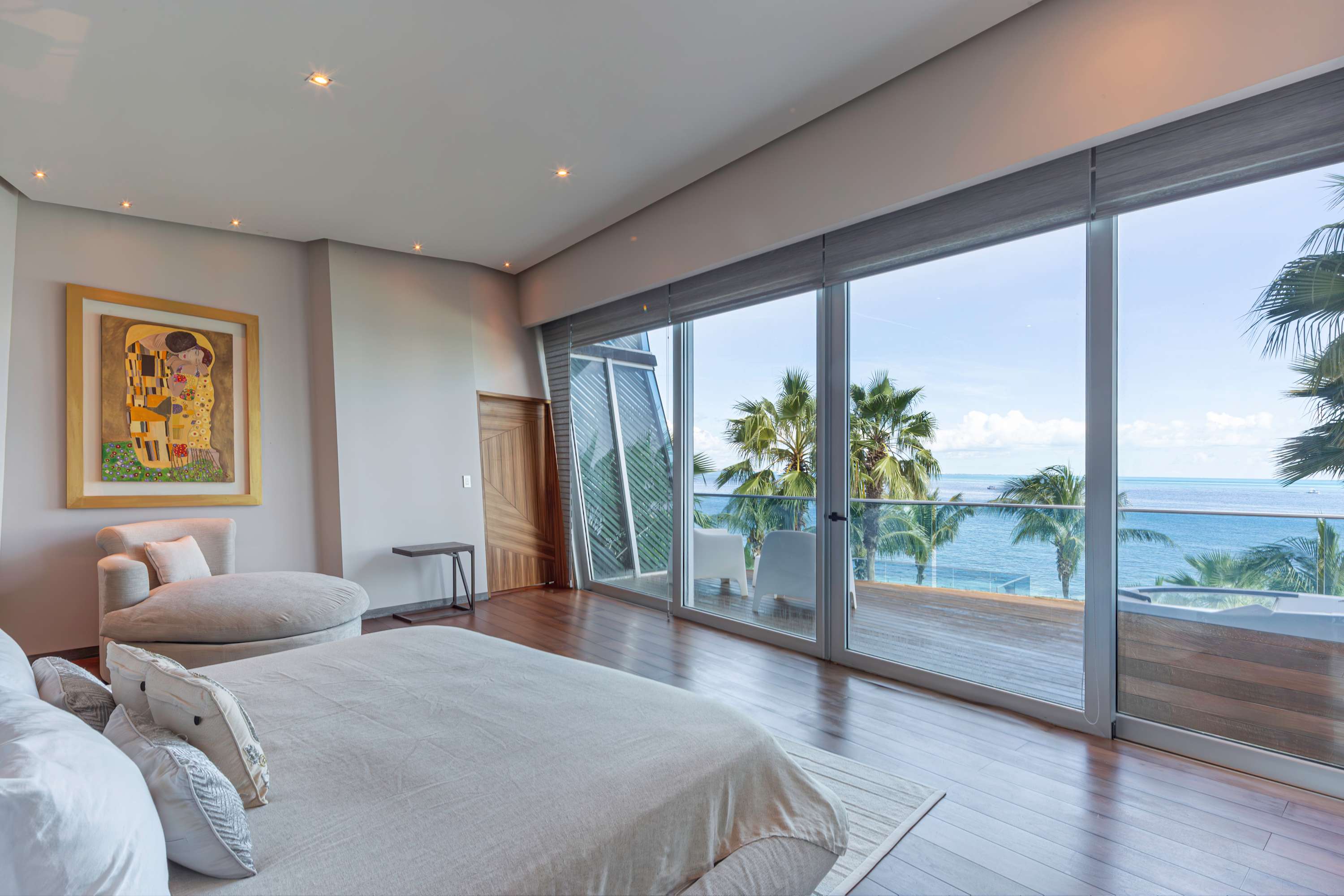 Bedroom with large glass doors opening to a balcony with ocean view and palm trees.