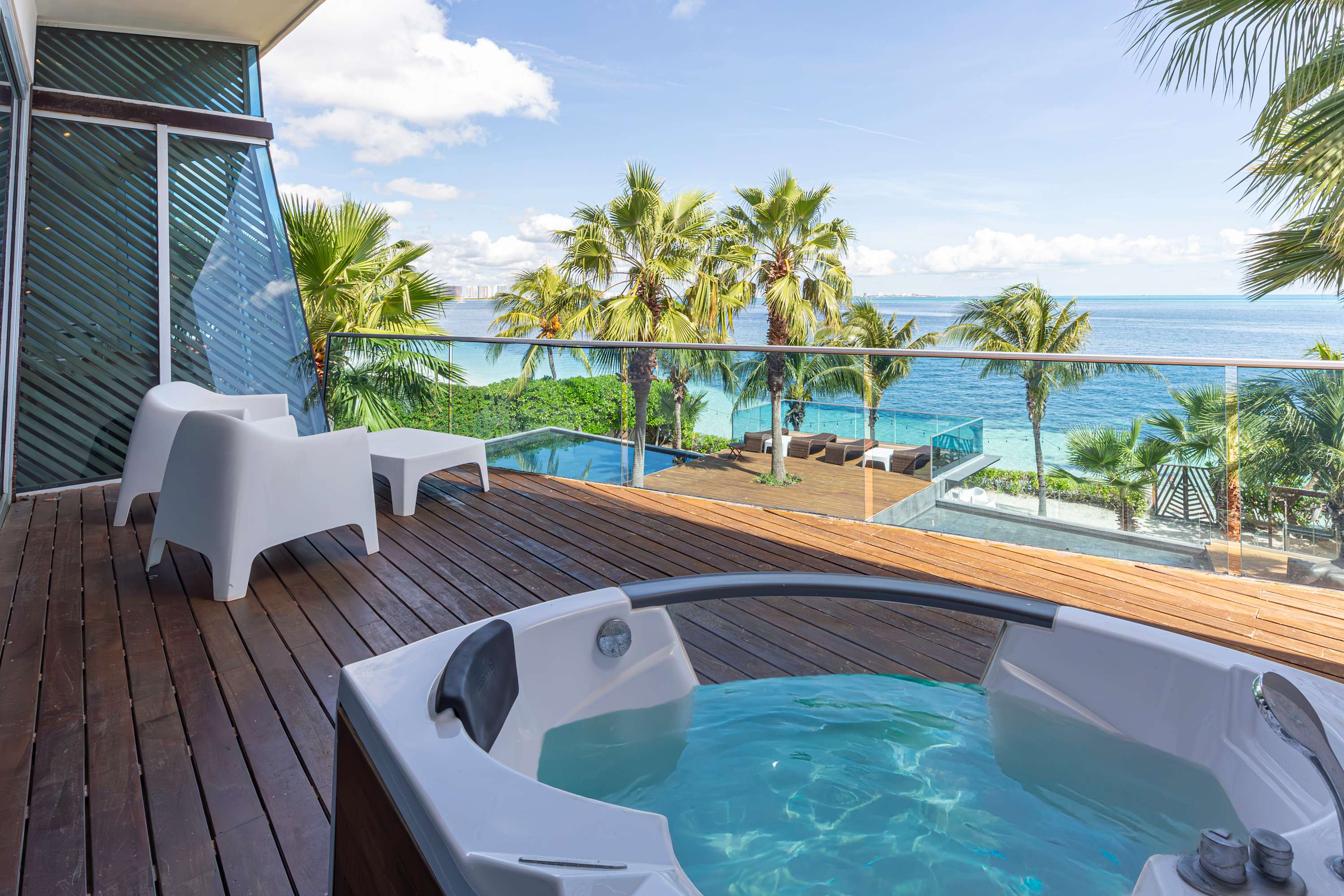A luxurious hot tub overlooks a stunning tropical ocean view with palm trees and a pool.